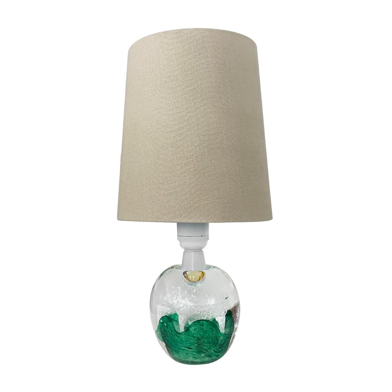 A small, late vintage Mid-Century modern Swedish table lamp with a new beige shade, made of colored Orrefors glass designed by Ölandshyttan in good condition. The inside of the Scandinavian slightly smoked apple shaped desk light is particularized