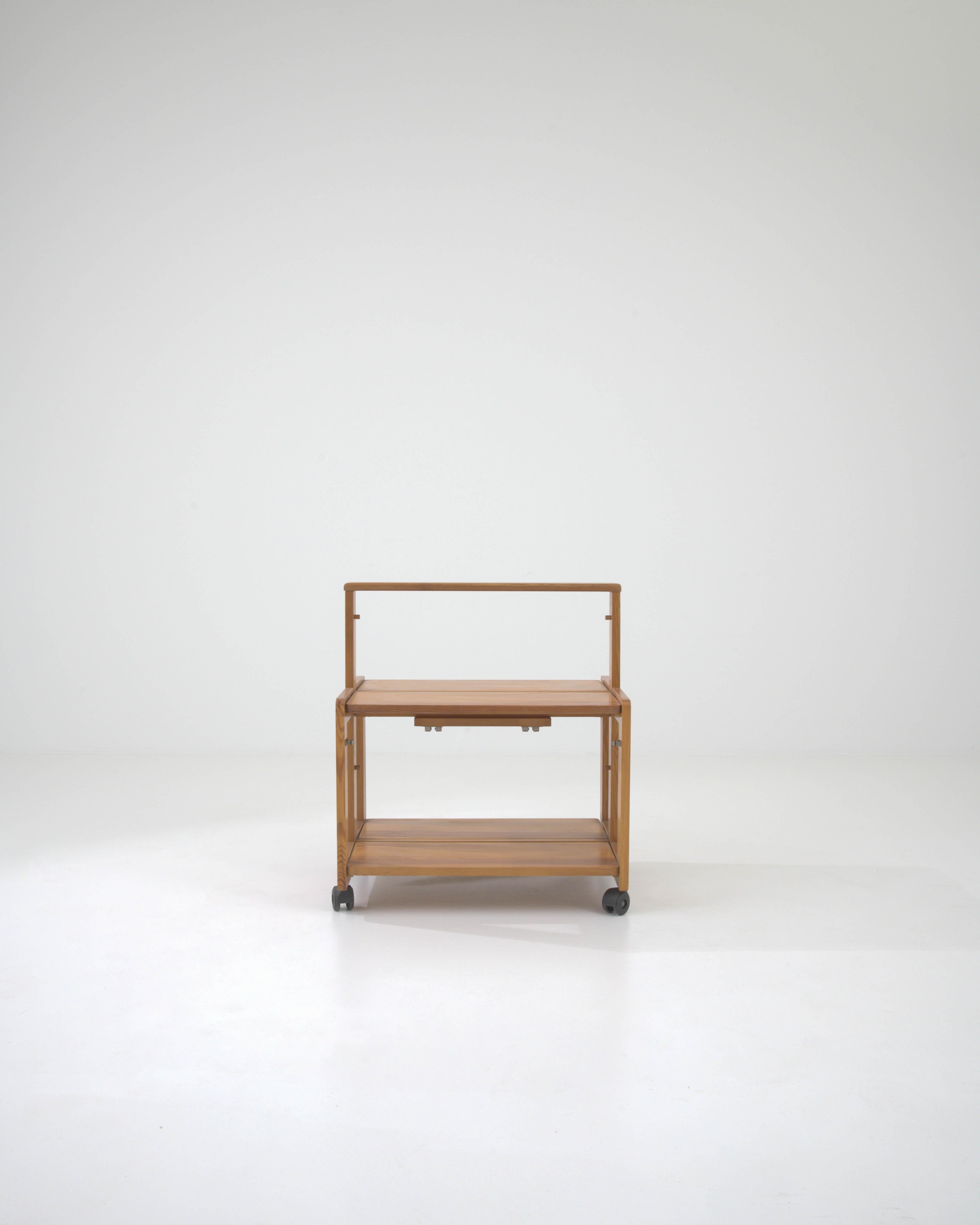 Experience the perfect blend of form and function with this mid-20th Century Swedish Wooden Bar Cart on Wheels. Its sleek, linear design showcases the simplicity and practicality that are hallmarks of Scandinavian craftsmanship. Constructed from
