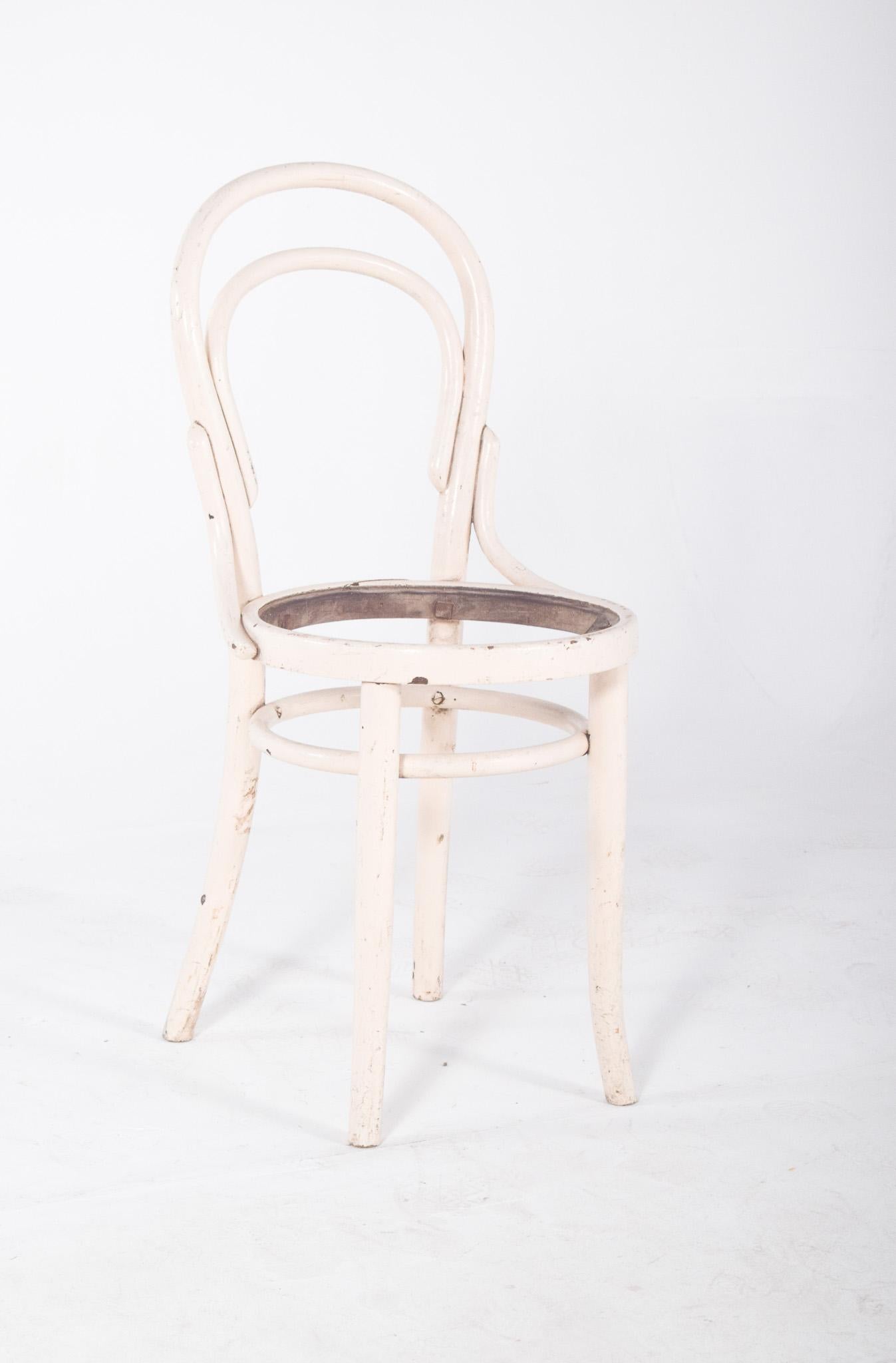 Thonet-style chair, painted white. With a low, curved backrest that extends laterally in a continuous, smooth line, characteristic of 20th century functionalist design. The structure has simple, discreetly curved shapes, with reinforcements under