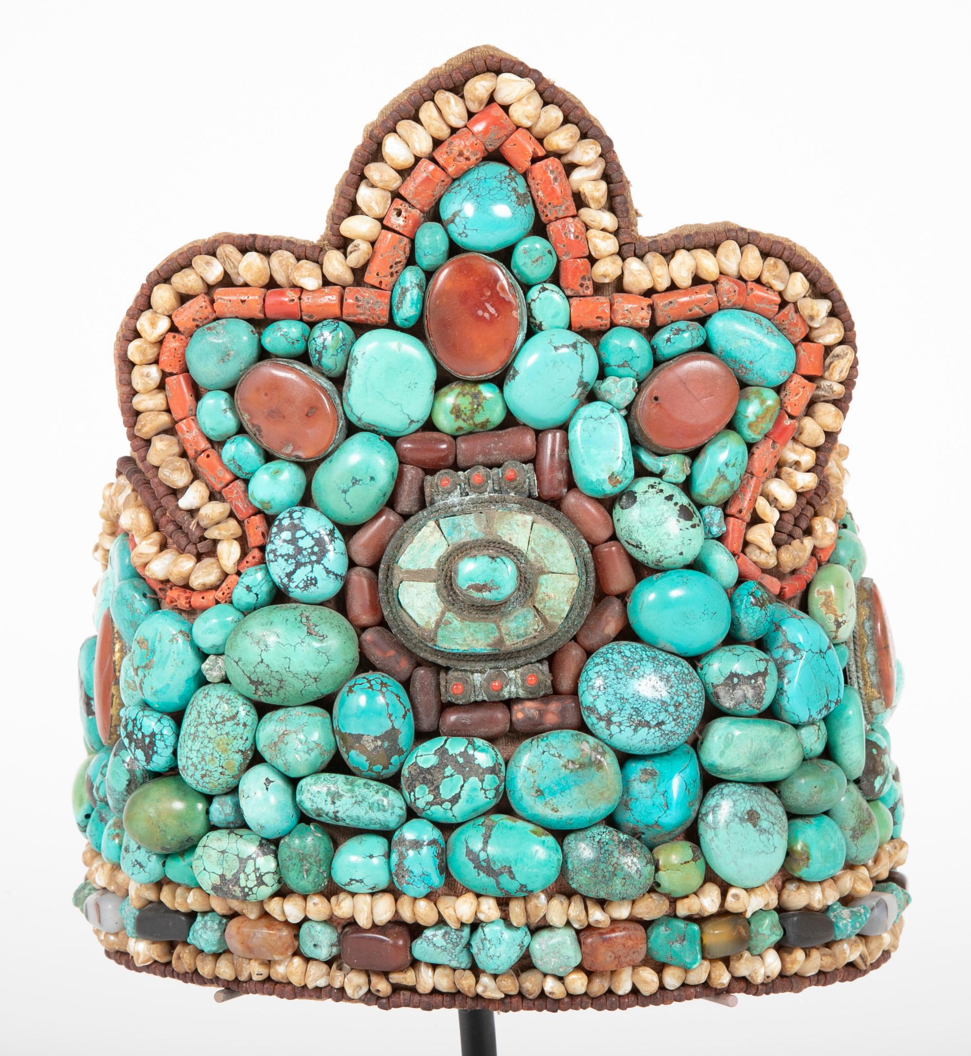 A traditional headdress from Ladakh featuring large beads of turquoise, nacre (mother-of-pearl ), and other semi-precious materials.  Mounted on custom metal stand.