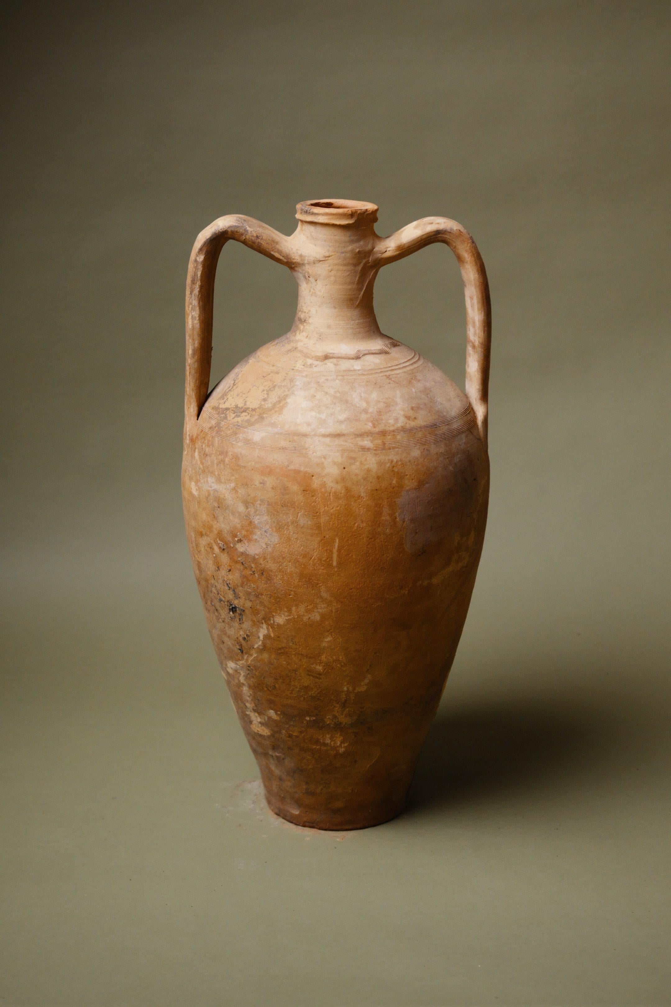 Un'anfora turca straordinariamente elegante, questo vaso di forma allungata incarna la ricca eredità dell'antico artigianato anatolico. Proveniente dalla Turchia, la sua forma snella e allungata con doppi manici graziosamente arcuati riflette il suo