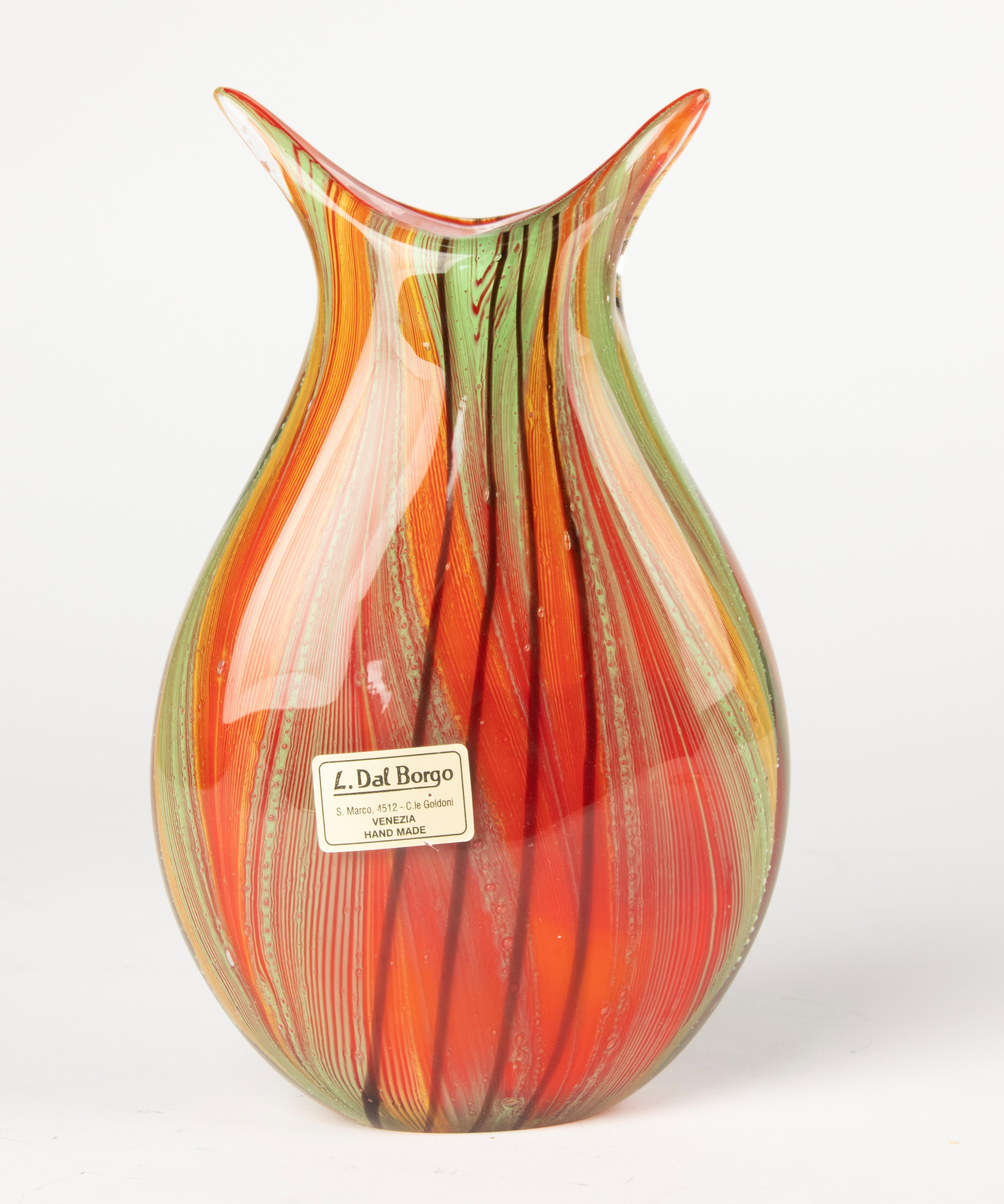 Vaso in vetro in stile Murano con una vibrante tavolozza di arancione, verde, giallo, rosso e nero in un motivo a strisce vorticose. Il pezzo mostra un'eccellente maestria, con un'armoniosa miscela di colori e una forma fluida e organica. Firmato