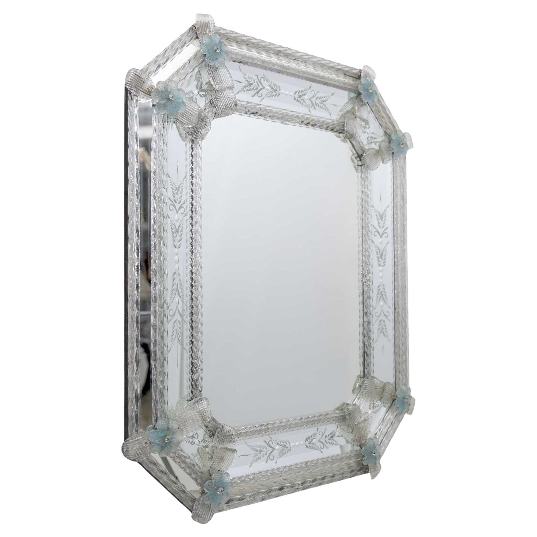 C'est un ravissant miroir vénitien classique avec un cadre formé par des baguettes et des boucles de cristal, les gravures qui ornent ce luxueux miroir ont été entièrement réalisées à la main, et les finitions composées de petites fleurs bleu clair