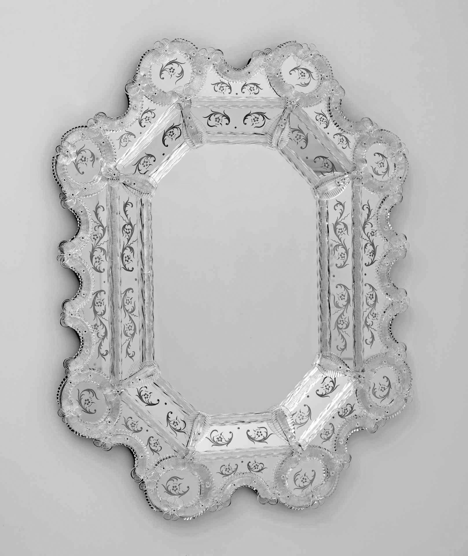 Il s'agit d'un ravissant miroir vénitien classique dont le cadre est formé de cannes et de boucles de cristal. Les gravures qui ornent ce luxueux miroir ont été réalisées entièrement à la main, et les finitions composées de petites fleurs et