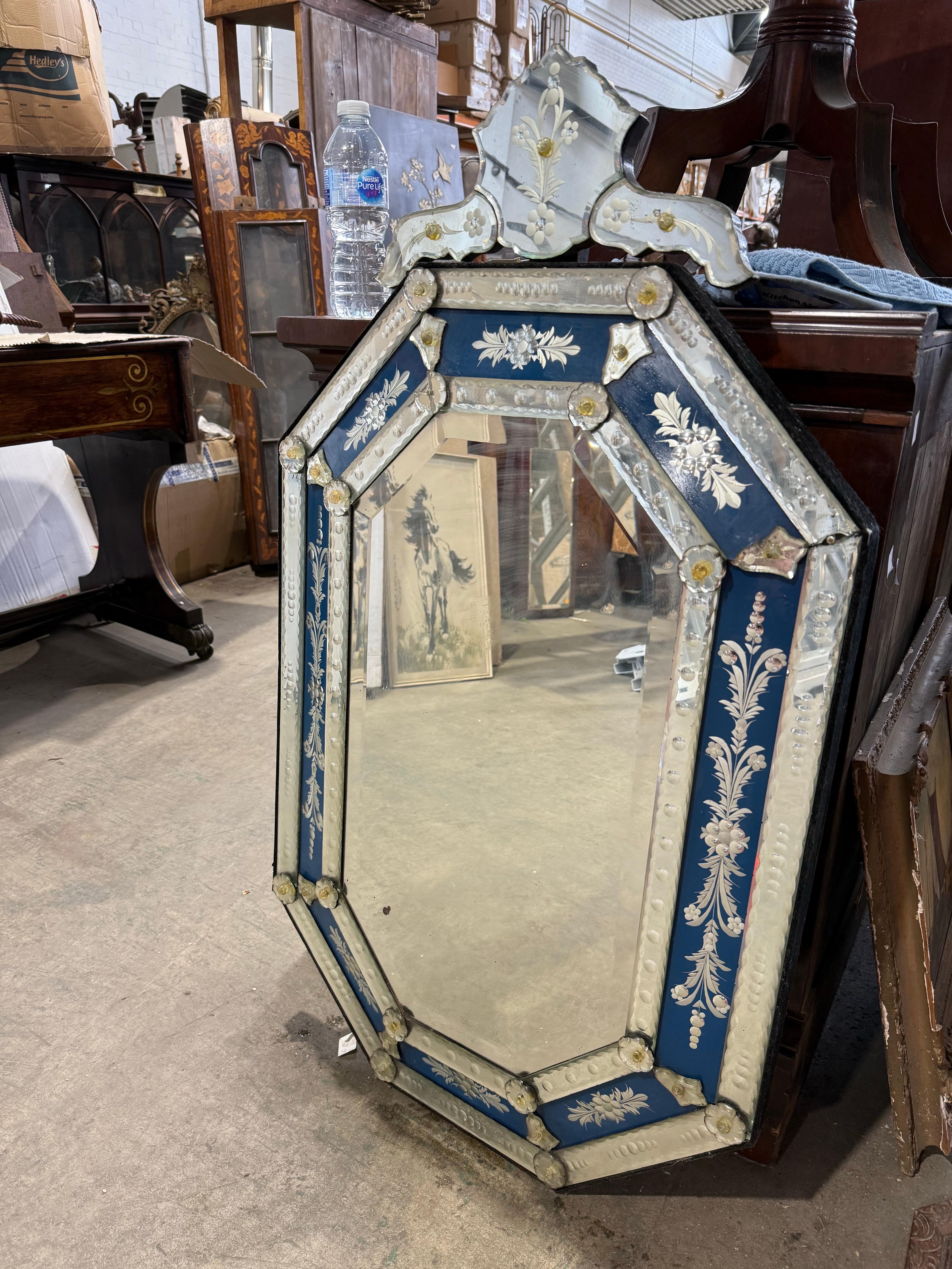 Exquis miroir vénitien du XXe siècle, de forme octogonale, encadré de panneaux floraux peints à l'envers (églomisé) dans de riches tons de bleu cobalt et d'argent. Chaque segment est individuellement biseauté et orné de motifs feuillagés
