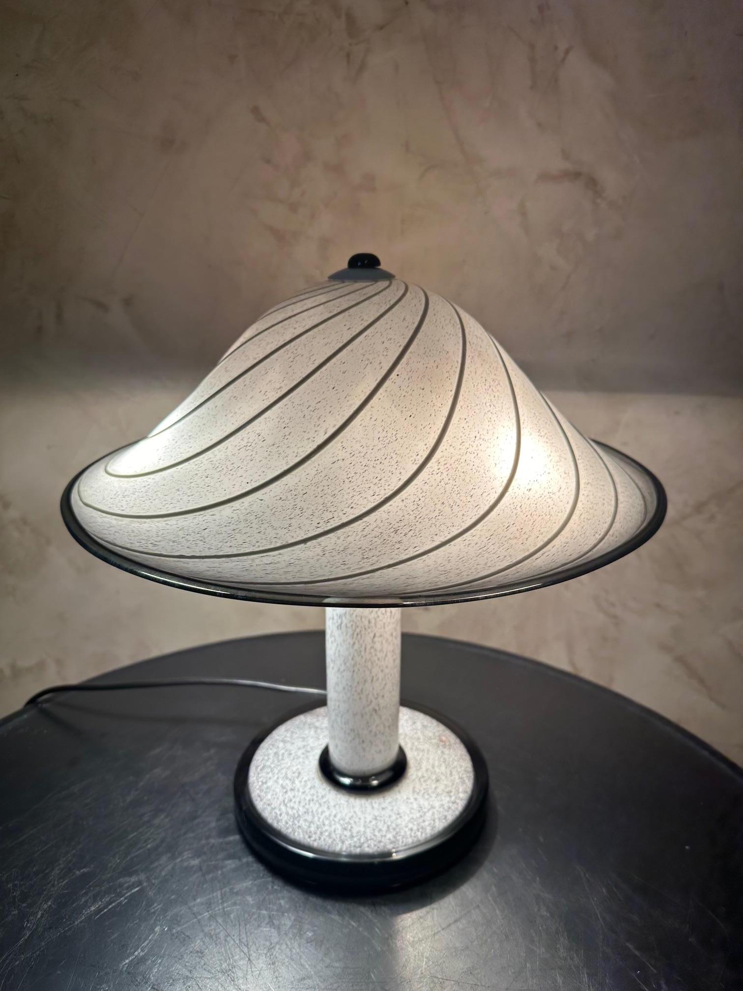 Magnifique lampe en verre de Murano datant des années 1950 en très bon état.
Couleur mouchetée de blanc et de noir. Abat-jour en forme de champignon. 
Trois ampoules à vis. Label du fabricant 