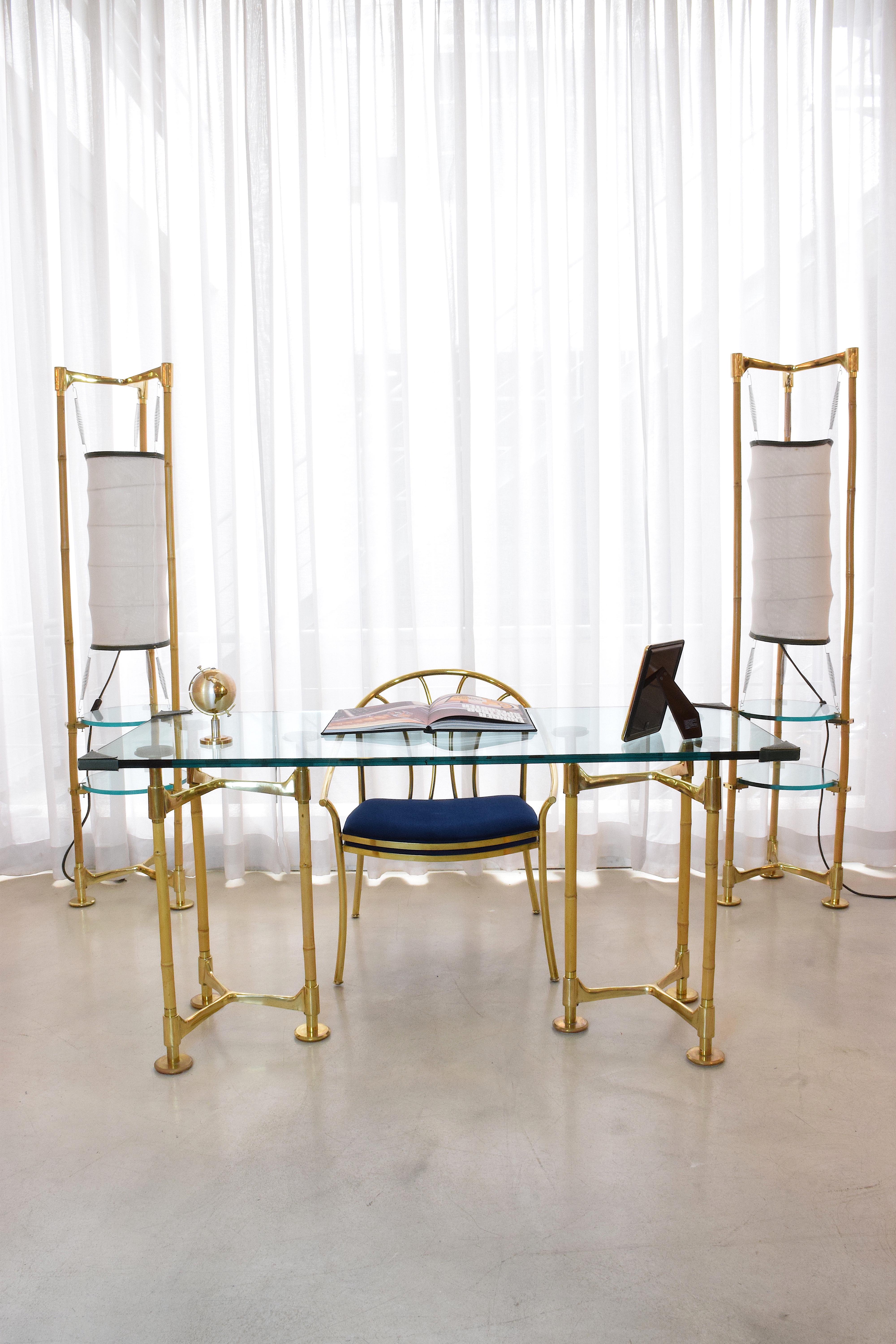 A stunning 20th century vintage rectangular desk composed of two tripod feet built out of gold polished brass and bamboo with circular disk endings. The tabletop is a 2cm thick glass and is adorned with leather stitched endings for