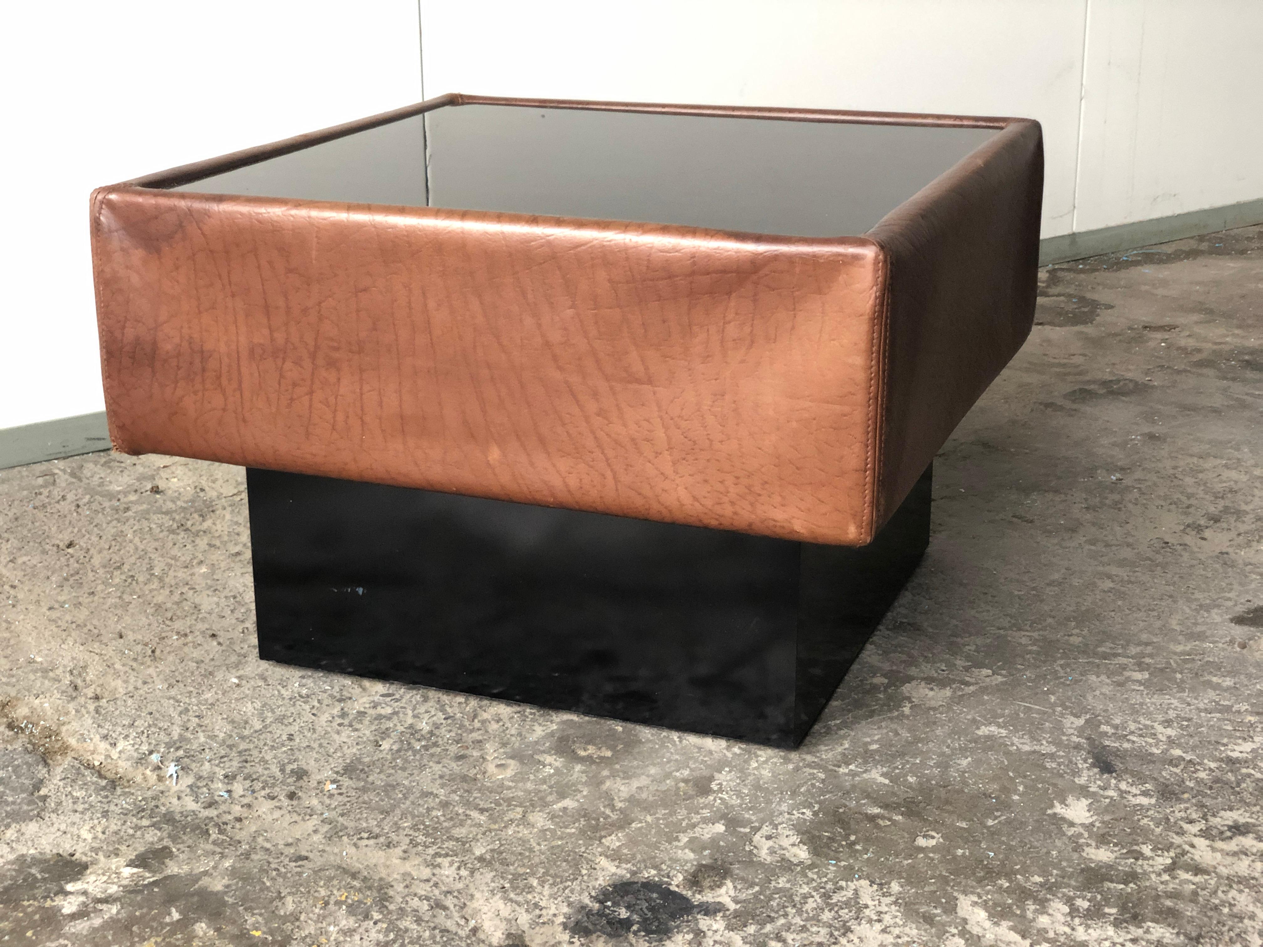 De Sede coffee table model DS1993 and pouf design from the 70s-80s, with graphic and geometric lines, structure upholstered in chocolate-colored leather adorned with a black mirror-effect glass top. 
 