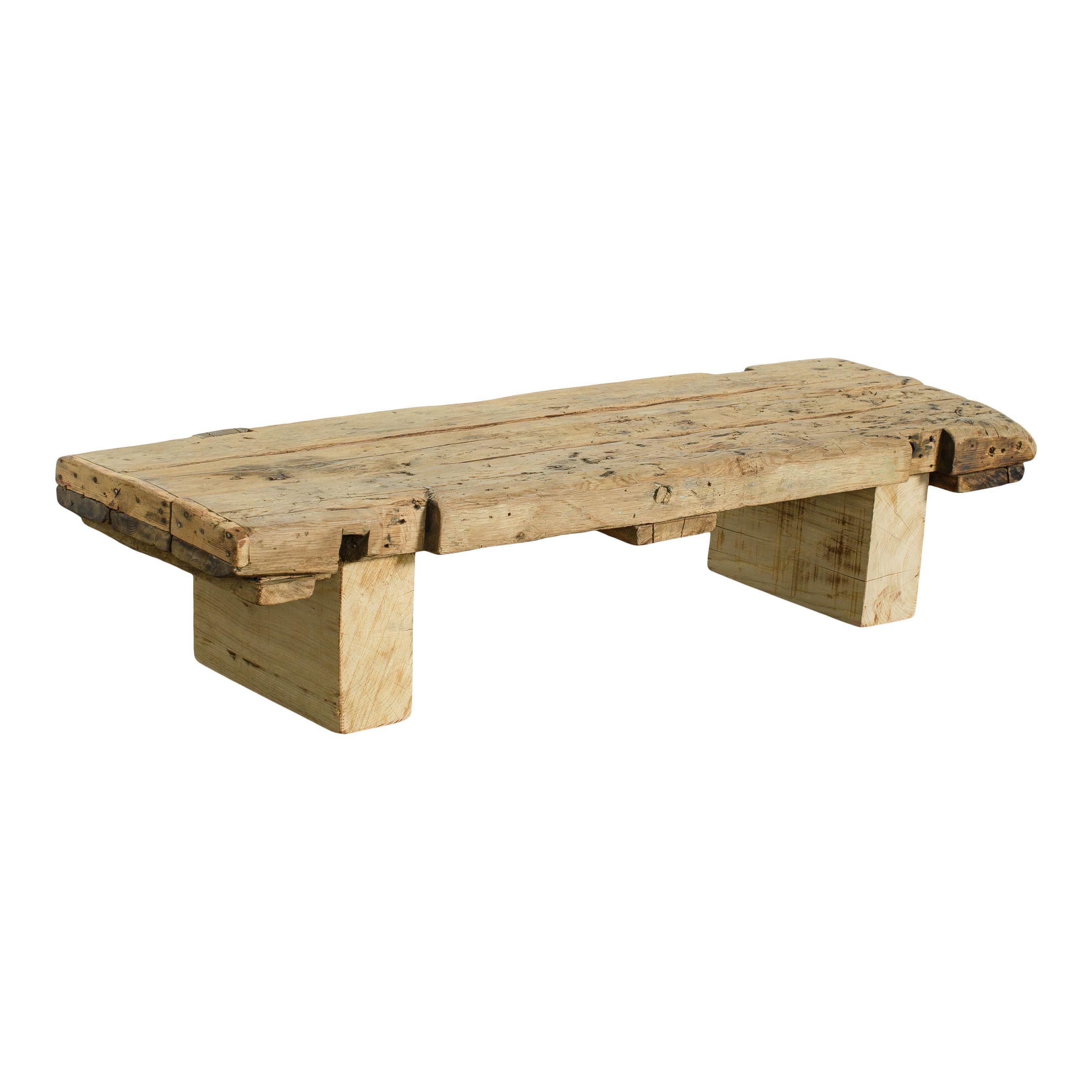 Table basse vintage en bois brut qui repose au ras du sol, importée de France. La forme et le toucher bruts de ce bois en font un ajout organique et naturel à tout espace. Il est composé d'un plateau et de deux pieds en bloc, le tout étant très