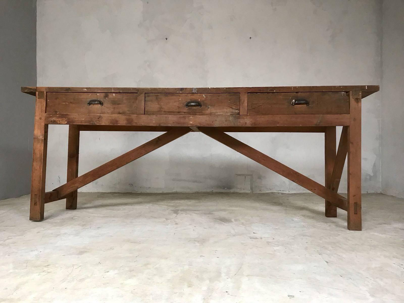 Great looking English pine workbench with three drawers and original black cast iron handles. It features an unusual and attractive base with cross bars below. This workbench was found in an old carpenter's workshop in the west of England and has