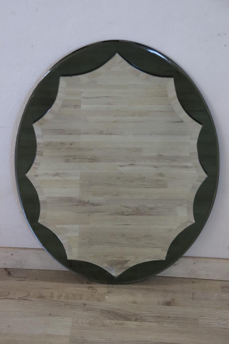 Schöner italienischer ovaler Wandspiegel aus dem 20. Jahrhundert, ca. 1960er Jahre. Der zentrale Spiegel mit gezacktem Profil ist an den Seiten fein geschliffen. Der ovale Rahmen um den Spiegel ist aus farbigem Glas gefertigt. Sehr speziell, perfekt