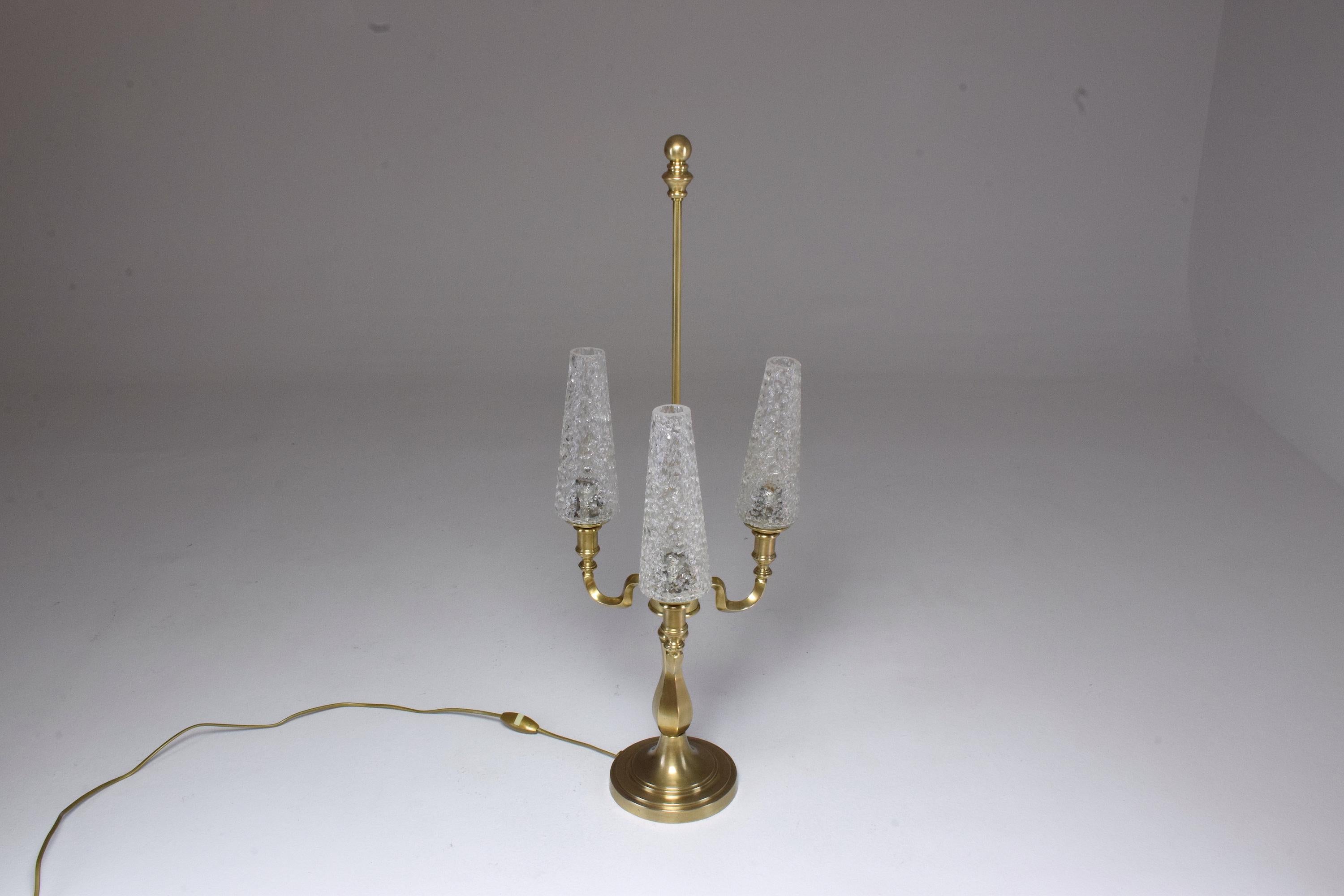 A 20th century vintage three-arm table lamp in Hollywood Regency style circa 1960s-1970s built with a heavy solid polished brass cast base and composed of its original three crackle glass shades which are screwed with metallic inserts. This striking