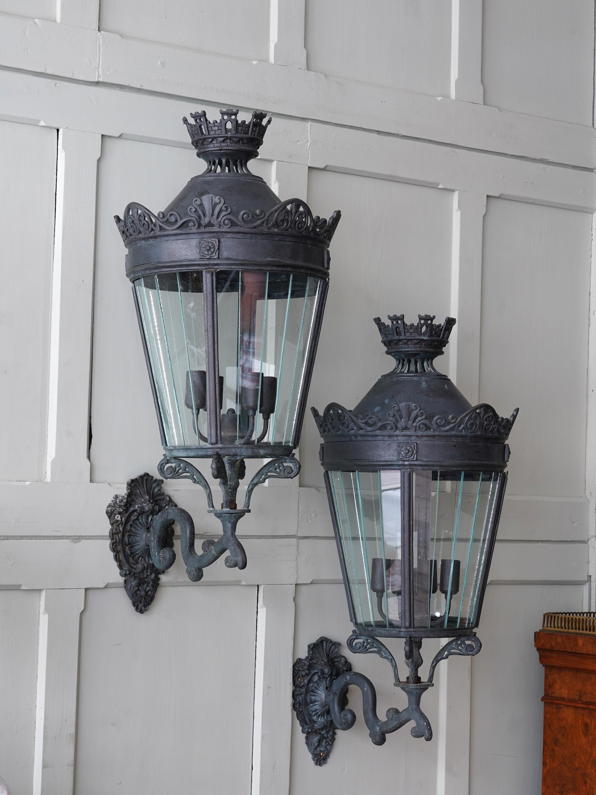 Ornate scrolling wall brackets supporting the glazed tapering cylinder with an Anthemion fringe below a castellated finial.

Three pairs available, price is per pair.

All rewired and PAT tested.