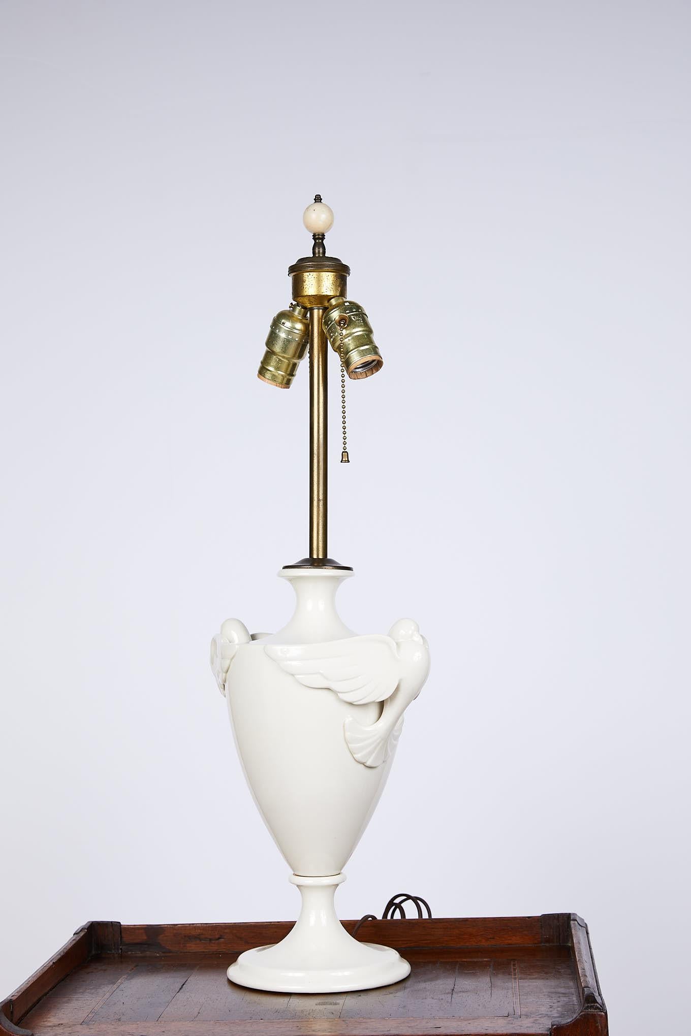 20th century table lamp in the Art Deco style made of white porcelain in a traditional urn shape with stylized doves mounted as handles on either side. 
 