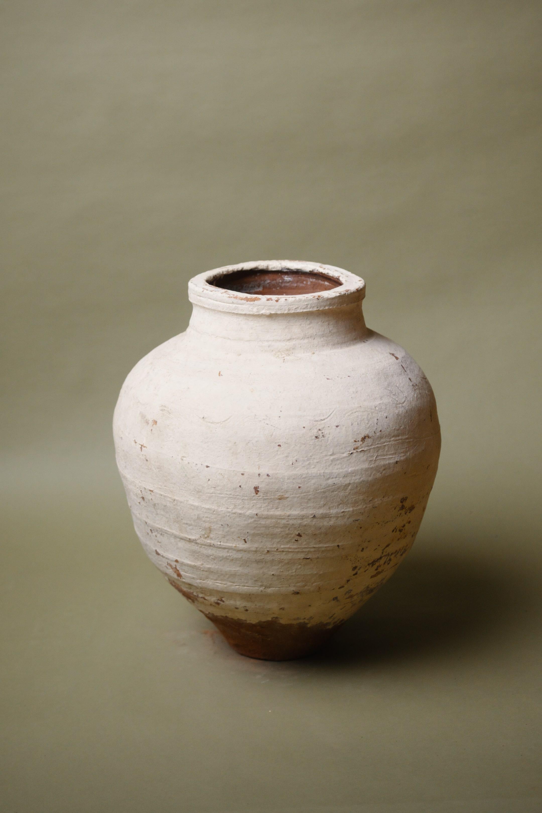 This 20th-century Anatolian terracotta jar is a testament to traditional craftsmanship, featuring a hand-applied whitewashed finish that beautifully contrasts its warm terracotta base. The soft, rounded form speaks to its functional origins, used