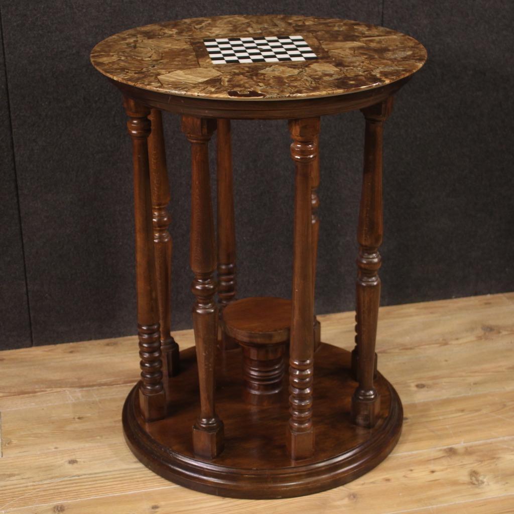 Italienischer Spieltisch aus der Mitte des 20. Jahrhunderts. Das Möbel wird von einer Holzstruktur mit einem runden Sockel getragen, der mit acht Säulen und einem kleinen zentralen Regal aus Kastanien- und Walnussholz ausgestattet ist. Top von