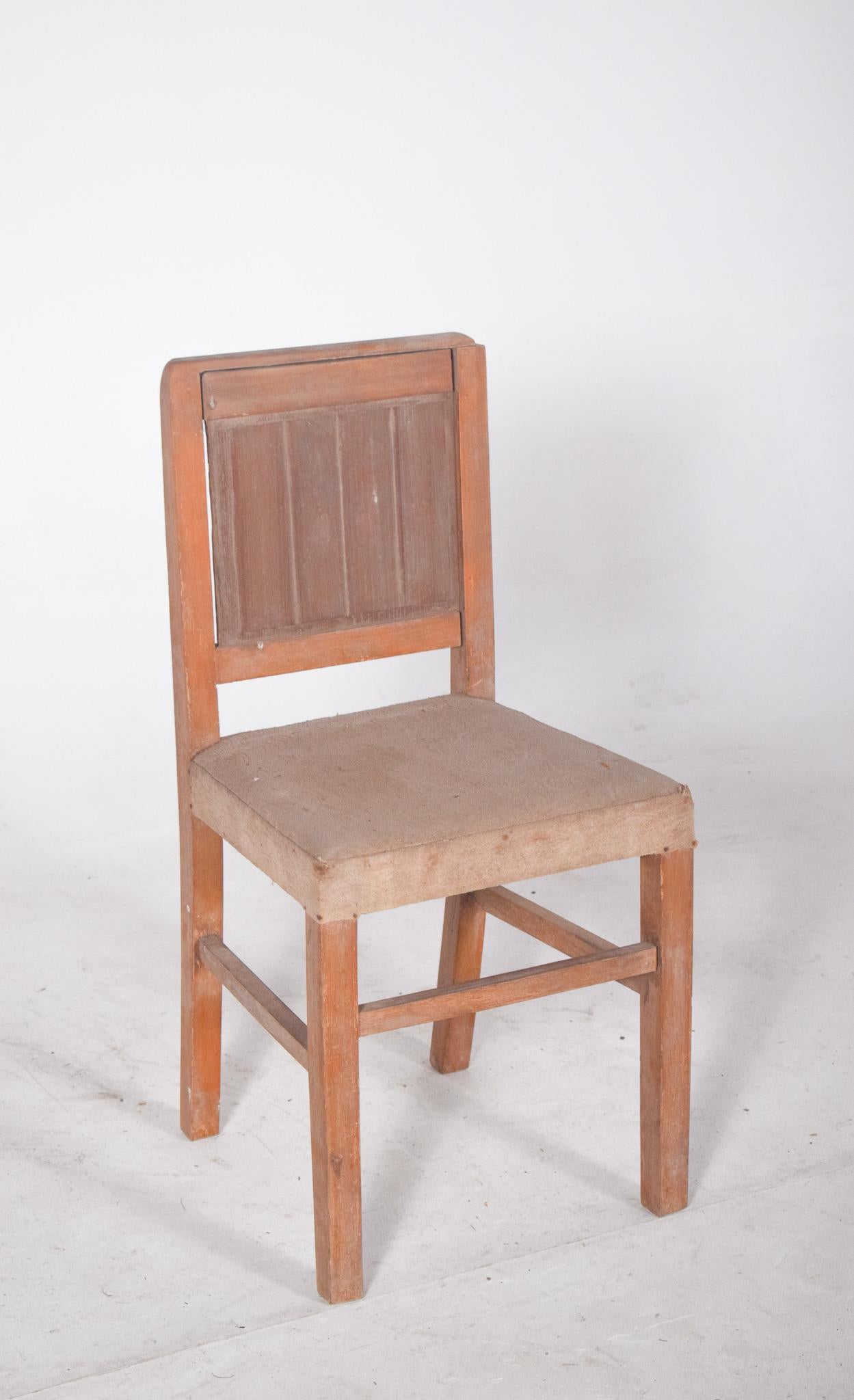 Silla de madera con tapicería beige. Respaldo y estructura de líneas rectas, de aspecto funcional y acabado rústico. El respaldo está compuesto por un panel vertical encajado en un marco con esquinas suavemente redondeadas. El asiento tapizado en