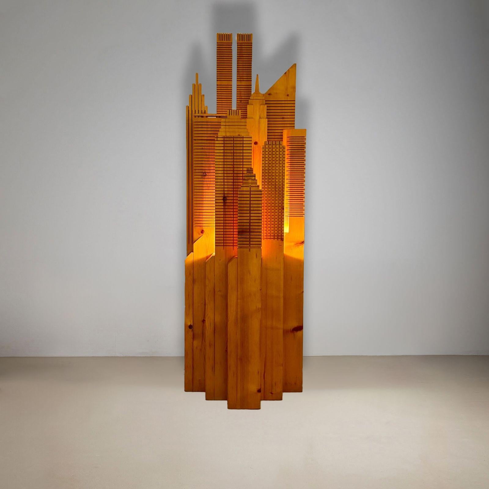 Questa drammatica e affascinante scultura illuminata da terra è scolpita in pino massiccio e raffigura i famosi edifici dello skyline di New York.  Tra gli edifici presenti: le Torri Gemelle, il Pan Am Building, la Citibank, Woolworth, Seagrams,