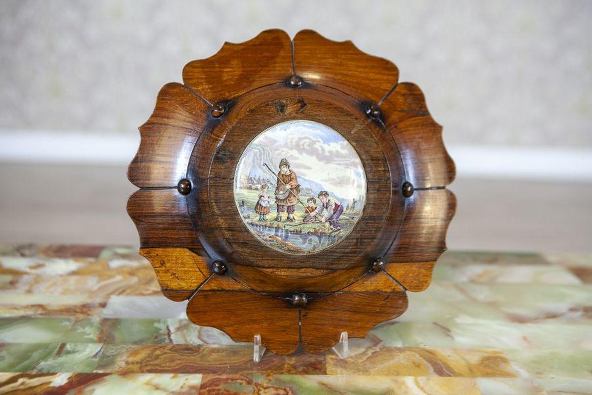 Decoración mural de madera de mediados del siglo XX con pintura de porcelana

Cuadro de porcelana que representa una escena de género, colocado en un marco decorativo de madera. En la parte inferior se ve una grieta reparada.