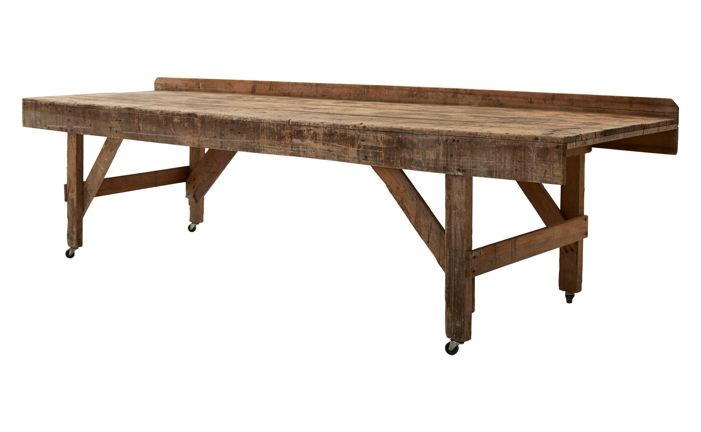 Made in America in the early 20th century, our industrial Vintage Work Table is crafted from patinaed wood, with caster wheels on all four legs. Although well-worn in appearance with many scratches and markings consistent with its age and use, this