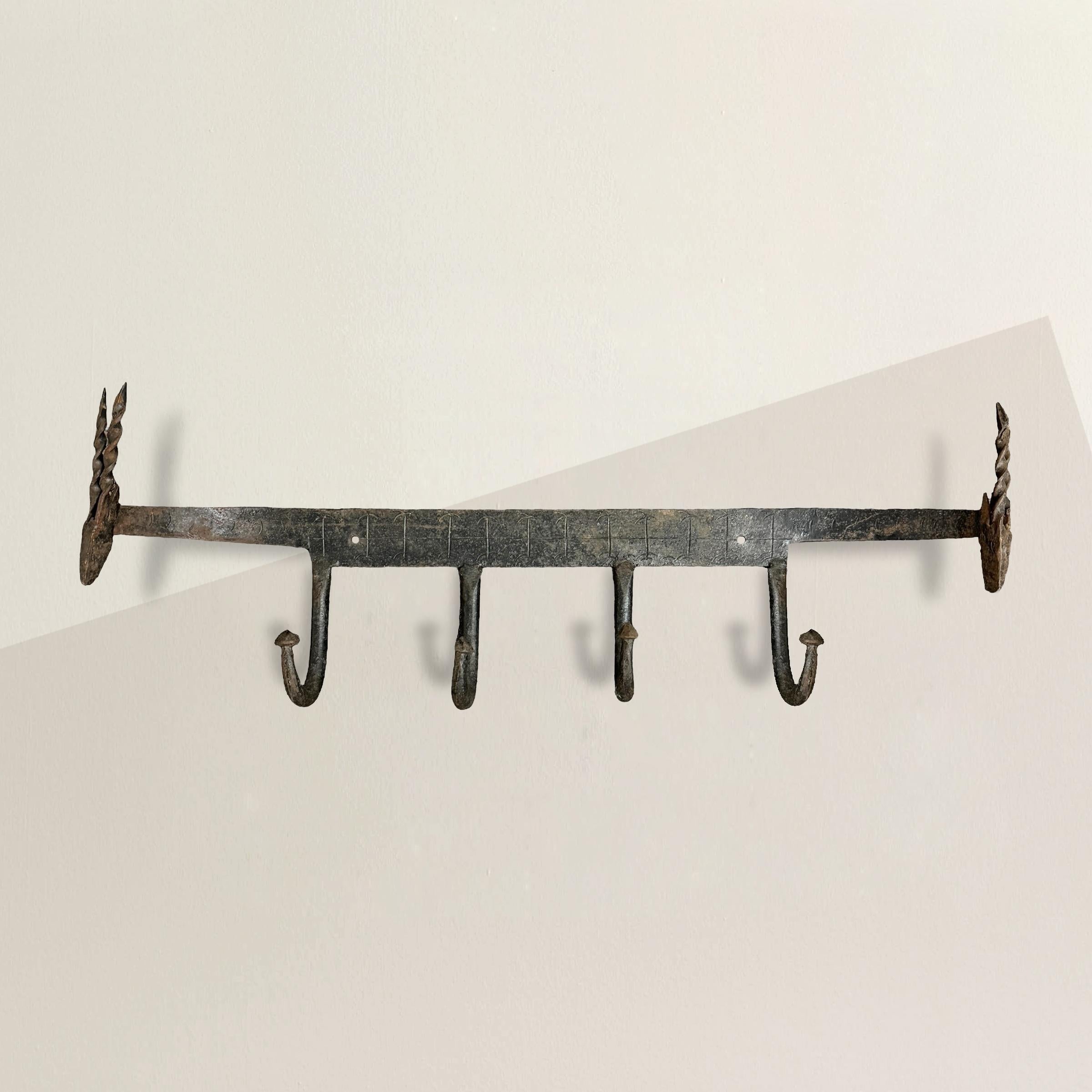 This 20th-century French hand-wrought wall-mounted hat or coat rack with four hooks combines functionality with artistic craftsmanship. Each end of the rack is adorned with a finely wrought iron antelope, their twisted horns adding a touch of wild