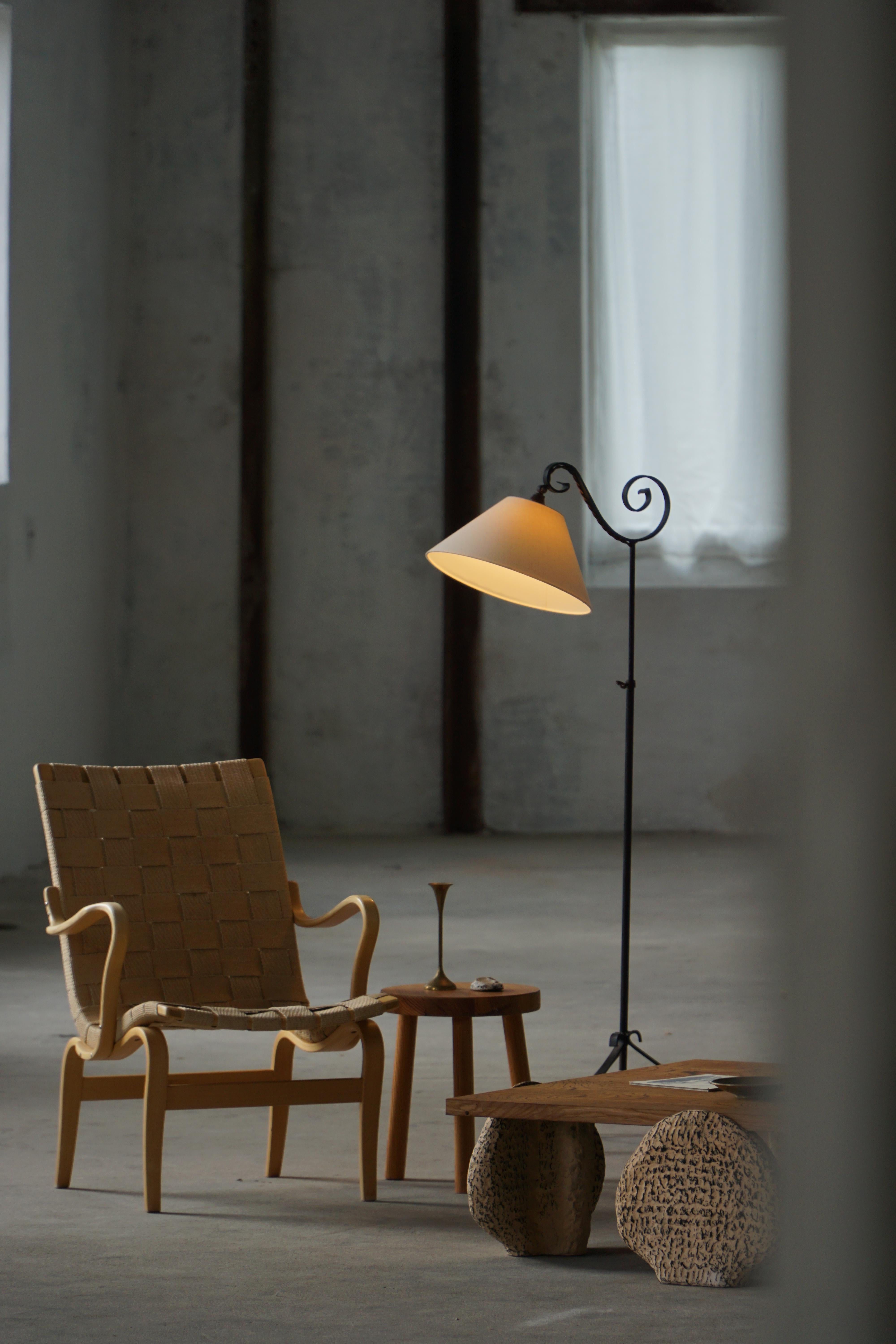A beautiful art deco floor lamp crafted from wrought iron, showcasing elegant artisanry and a sculptural presence. The lamp features a distinctive “swirl” design near the shade, adding a dynamic sense of movement to its otherwise clean and minimal