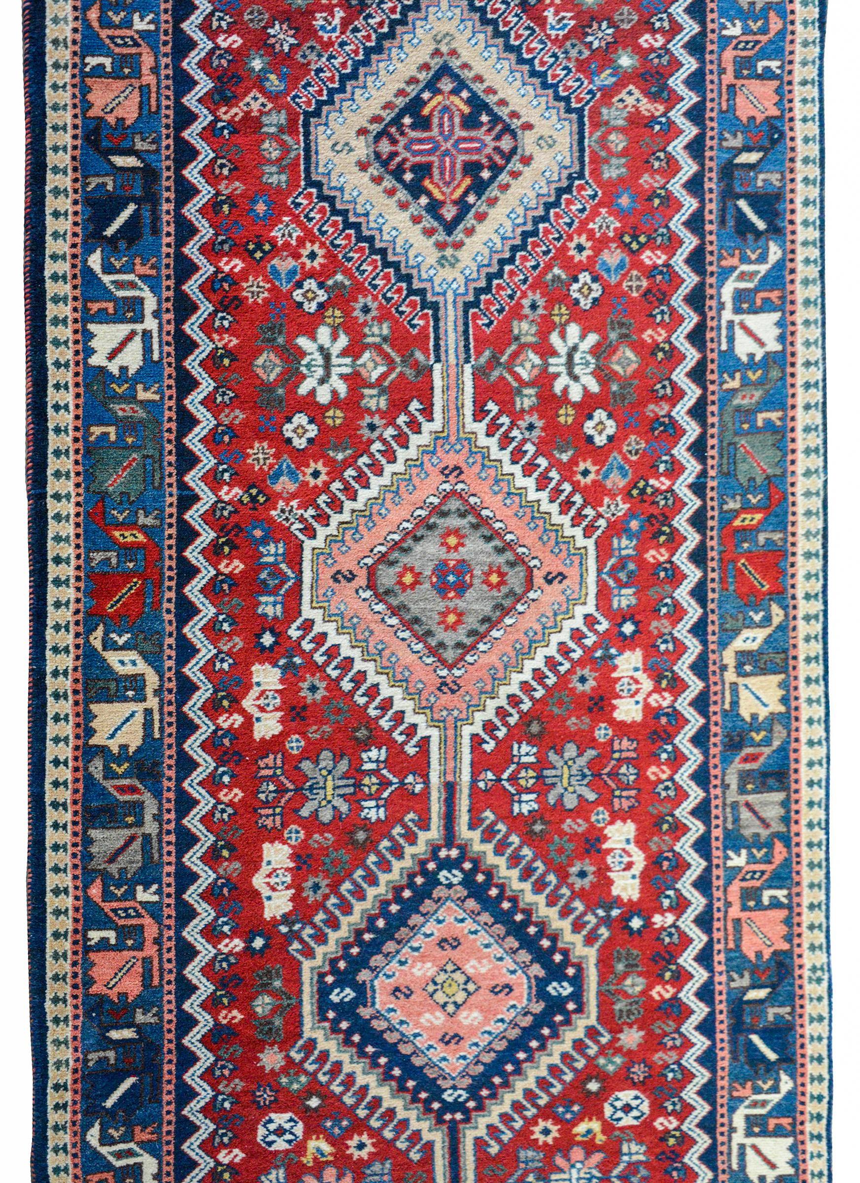 A bold 20th century Persian Yalameh runner with eight multicolored diamond-shaped medallions amidst a beautiful crimson field of flowers and surrounded by border with a stylized multi-colored floral border against an indigo background.