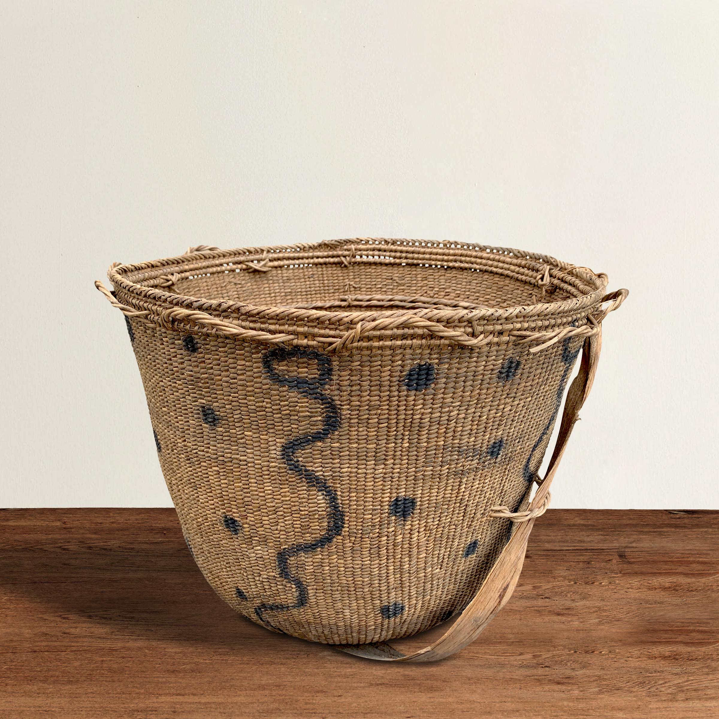 A 20th century Yanomami gathering basket decorated with charcoal drawn circles with snake-like figures and dots on the exterior. This basket is tightly handwoven of natural fibers with several inner rings for stability. The straps are tied around