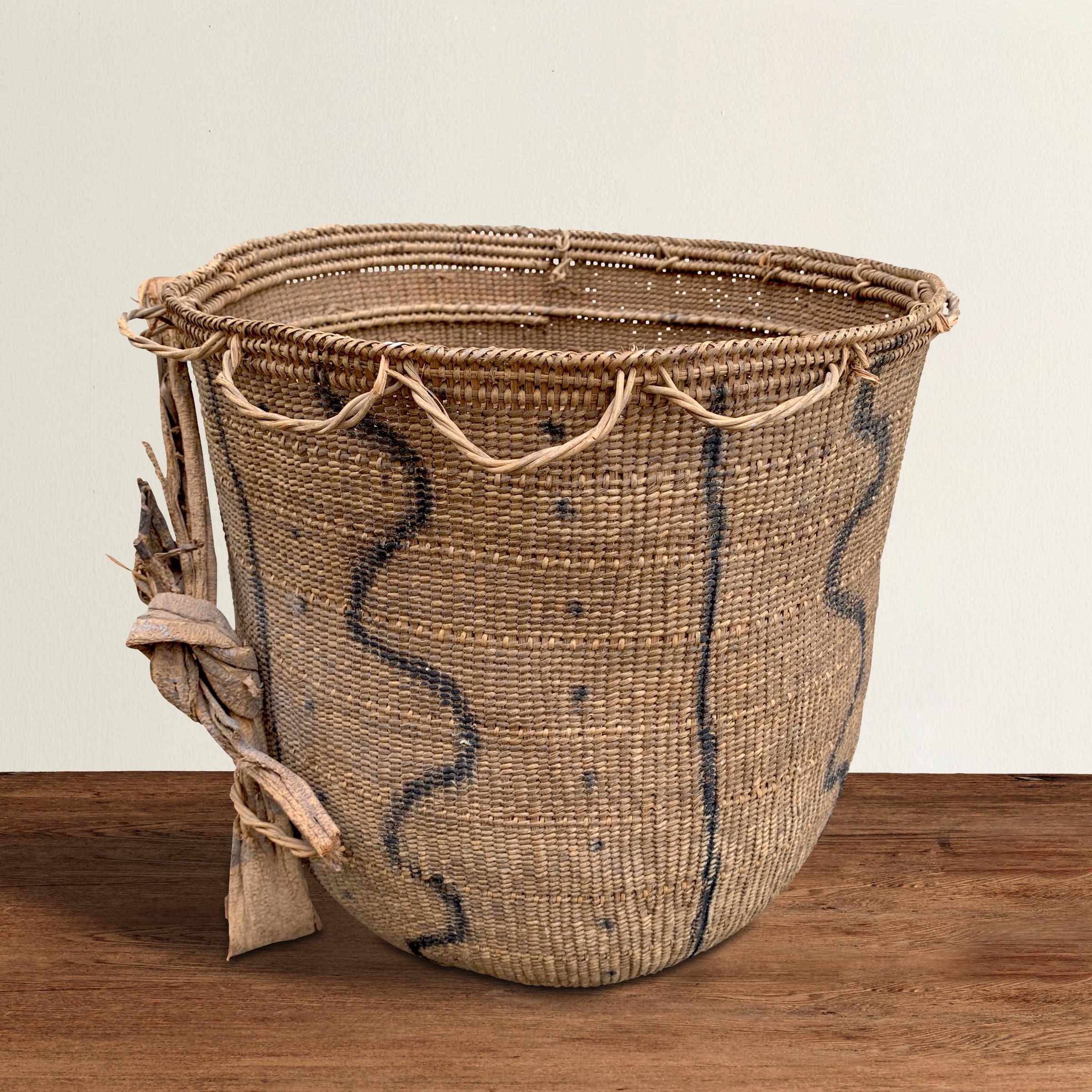 A 20th century Yanomami gathering basket decorated with charcoal drawn circles with lines reminiscent of rivers and dots on the exterior. This basket is tightly handwoven of natural fibers with several inner rings for stability. The straps are tied