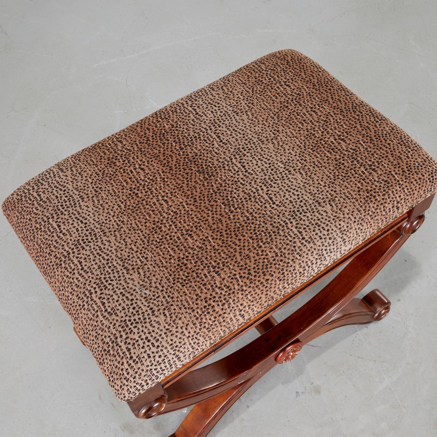 Late 20th c., an English Regency style curule bench upholstered in a subtle animal print, unmarked. X-frame legs and base each terminating with scroll detail. Squared off at corners. Decorative brass upholstery nail head trim around the seat