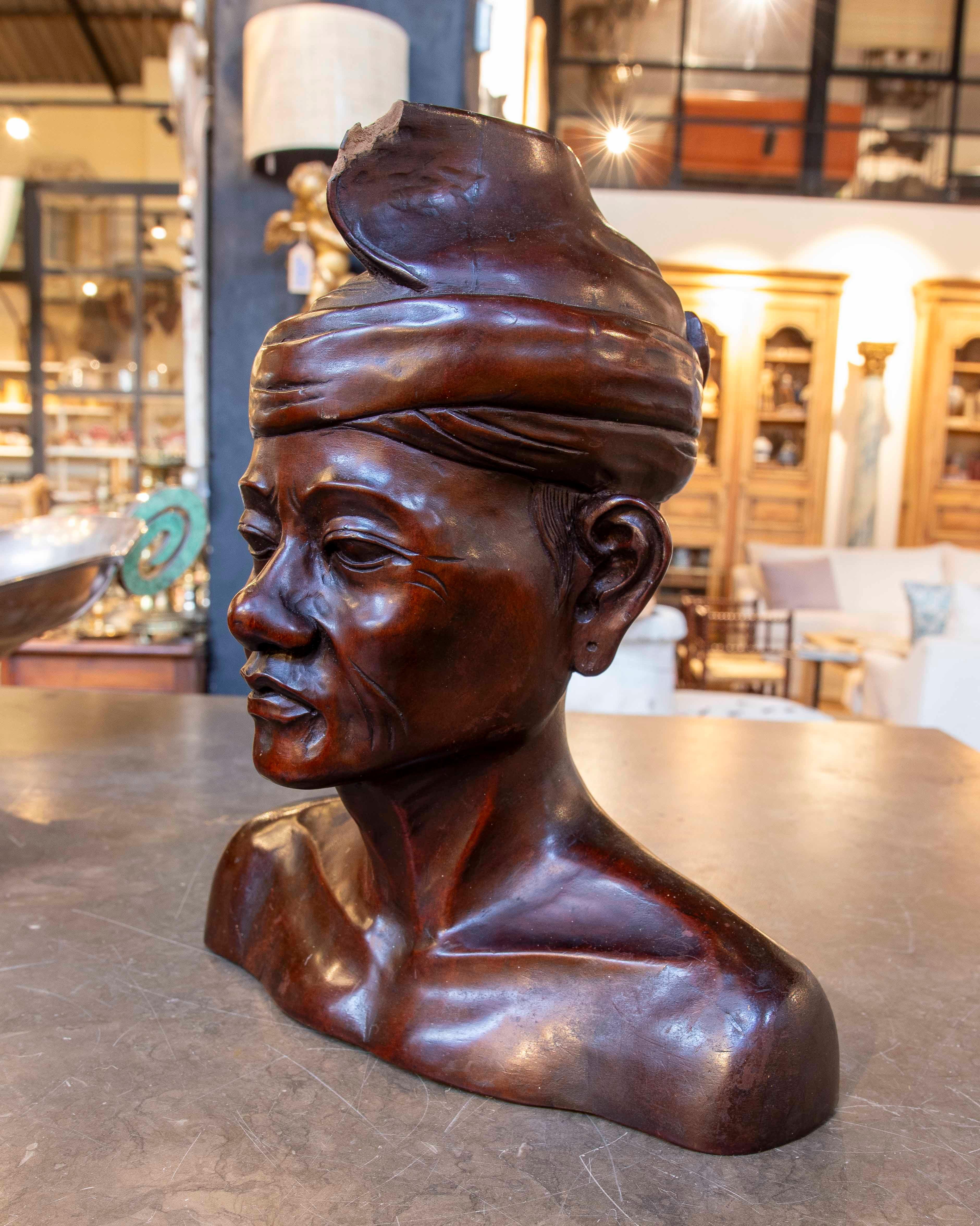 Impressive hand-carved wooden bust, representing a man with a turban, characteristic of traditional Asian art. The piece stands out for its level of detail, capturing realistic facial expressions and a careful texture that highlights the artisanal