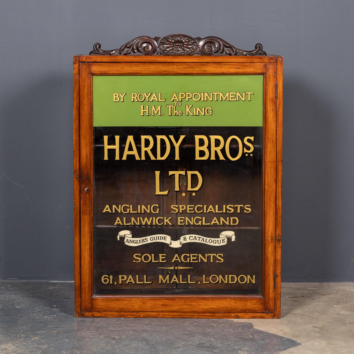 Antique early-20th century English glass & mahogany shop display cabinet with brass edges on a wooden stand. A small counter top display cabinet is later sign written for the famous Hardy Brothers angling specialists with rear access and two glass