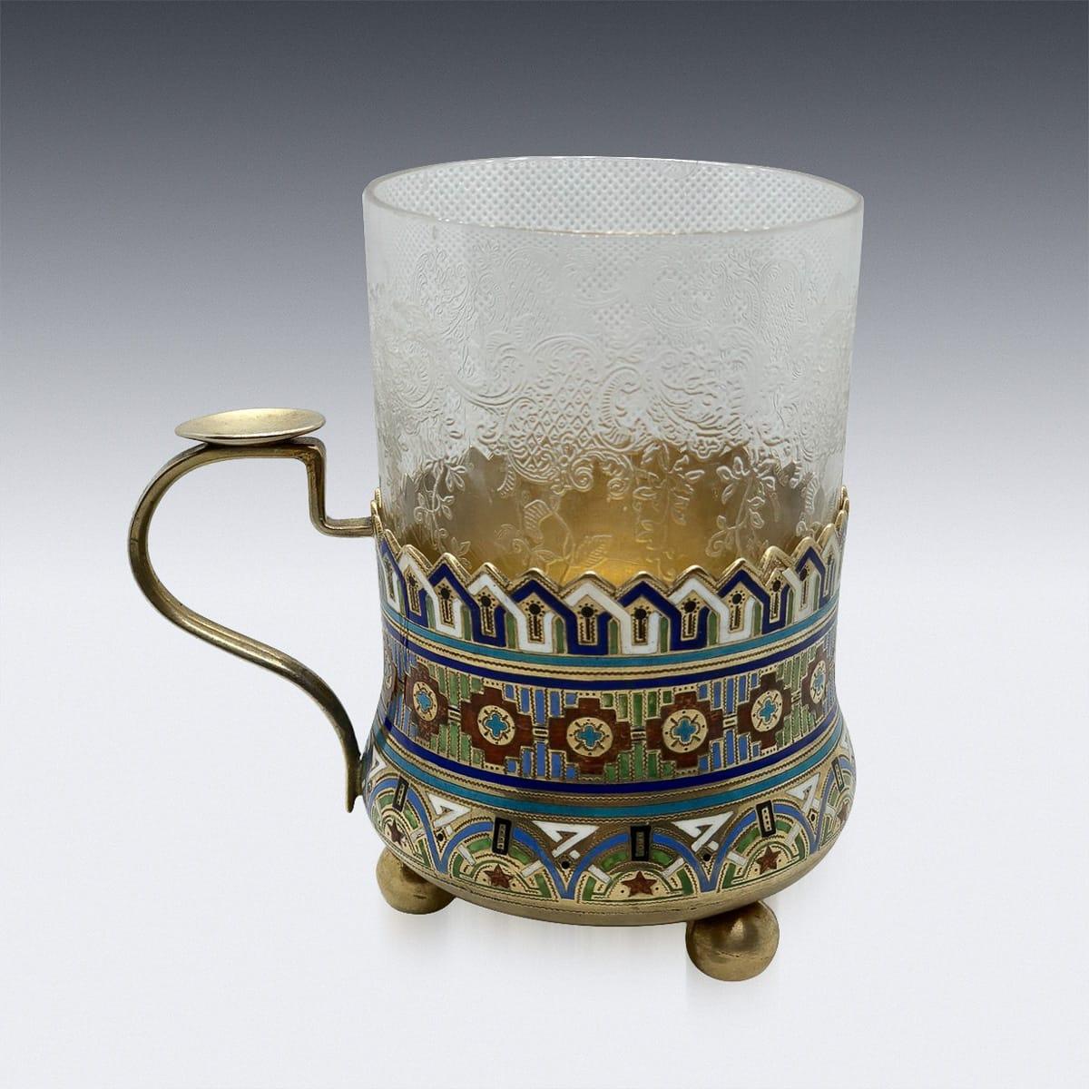 Antique early 20th century Imperial Russian solid silver-gilt and champleve enamel tea glass holder, circular with a plain handle mounted with a thumb-rest, standing on three ball feet, the body profusely decorated with pan-slavic geometric motifs