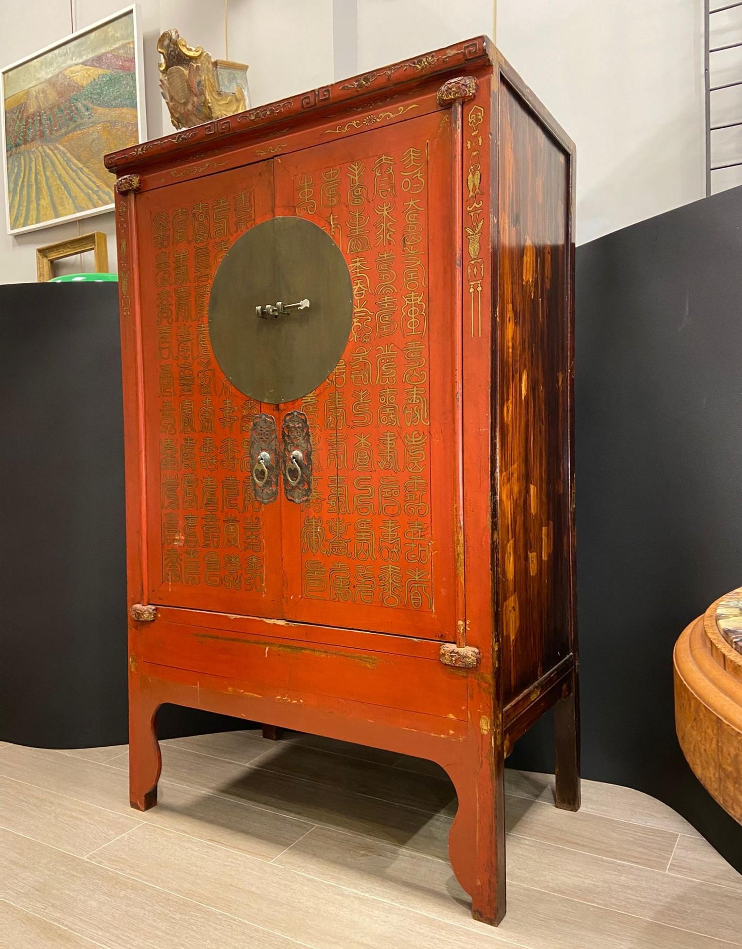 Magnifique cabinet chinois réalisé vers 1900 en bois d'orme laqué rouge, et décoré à la main à la poudre d'or. Les ferrures et le trou de serrure sont en fer d'origine de l'époque. Ce magnifique meuble possède également un ornement sculpté dans le
