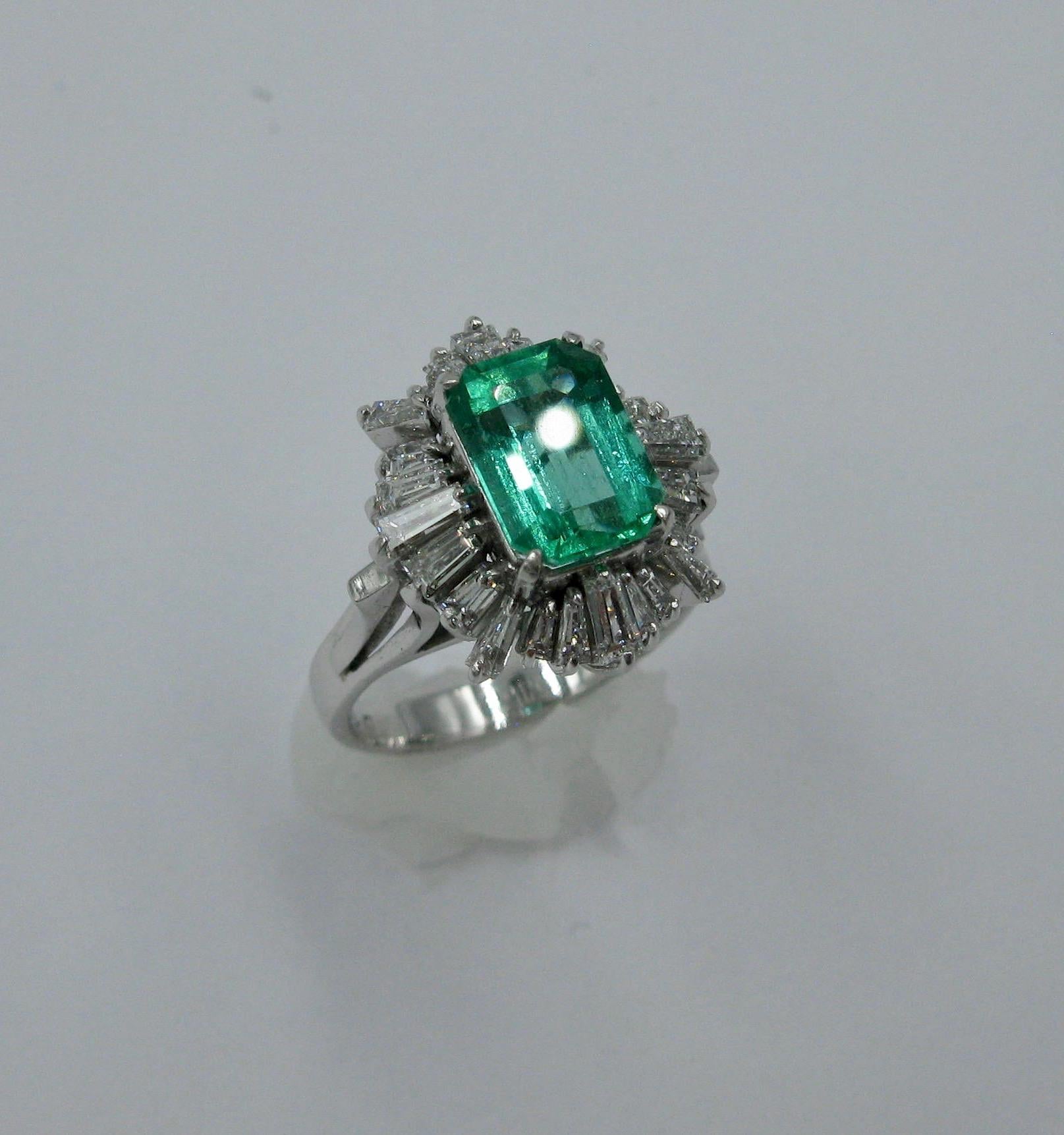 This is a stunning cocktail ring with a 2.1 Carat Emerald Cut Emerald of great beauty surrounded by 24 brilliant white Tapered Baguette Cut Diamonds totaling 1.2 Carat all set in Platinum.  The jewels are of superb quality.  The halo effect of the