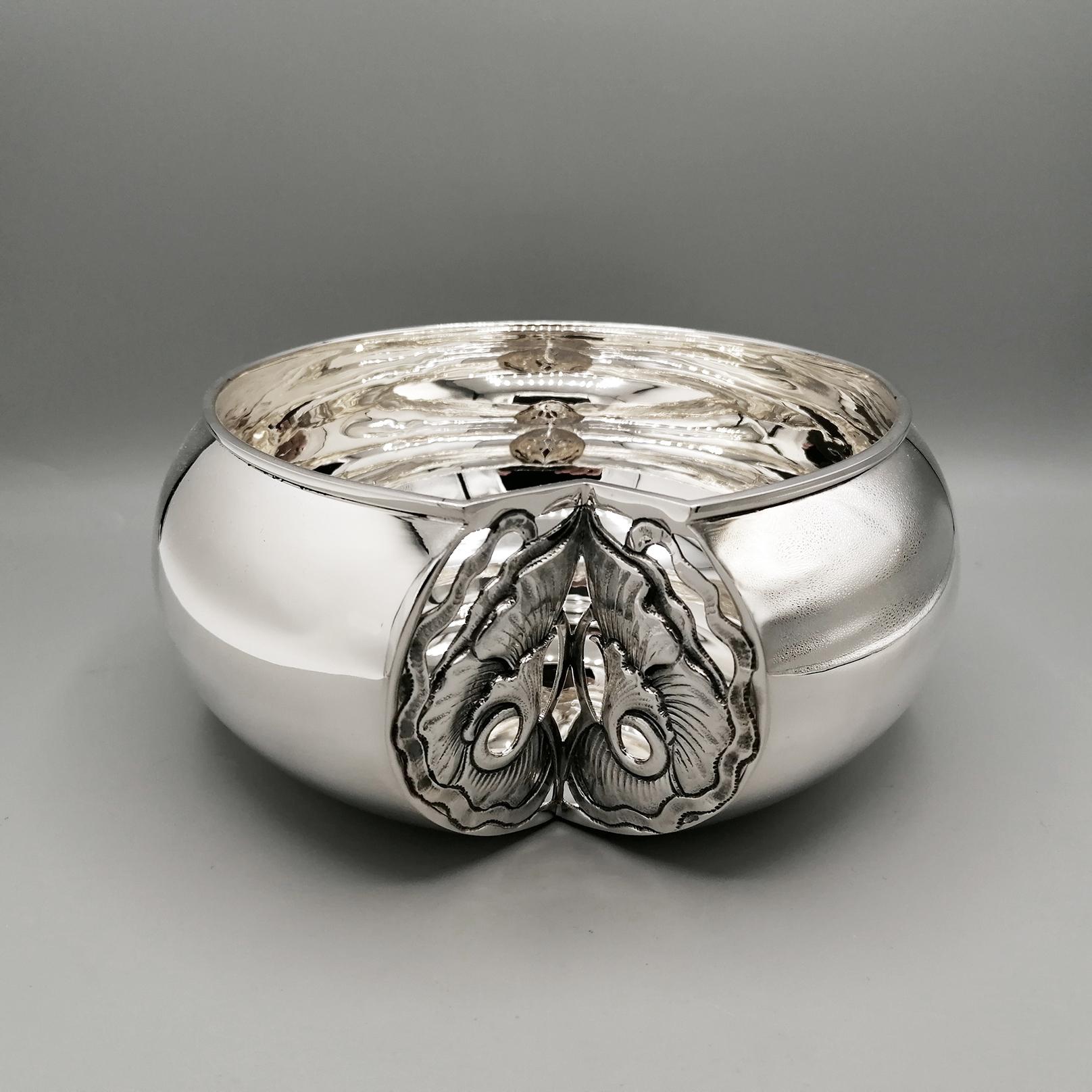 Round shaped sterling silver bowl.
The edge of the body of the bowl is markedly domed and abruptly interrupted by a section cut toward the inside of the triangular-shaped object.
A plaque with flowers, made with the fusion technique, was welded into