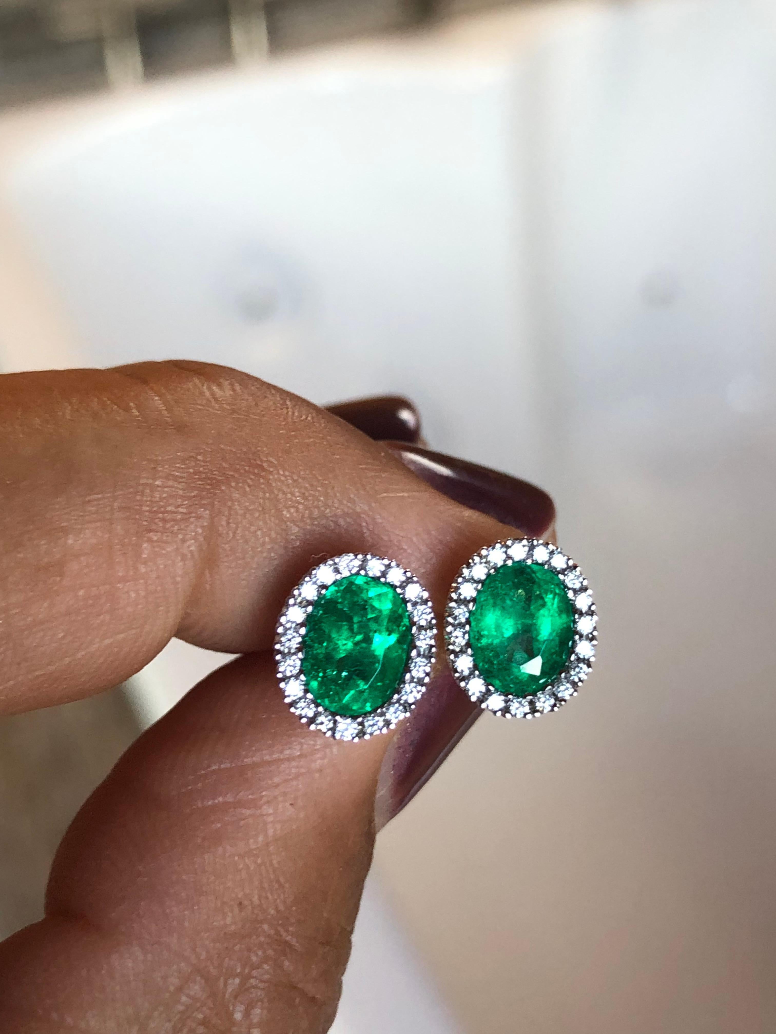 A stunning pair of 1.90 carats, AAA+ vivid green color, lustrous, transparent fine natural Colombian Emerald earrings with a diamond halo surrounding it, all set in 18K White Gold.  
Stone: Colombian Emerald  Weight: 1.90 carats  
Shape: Oval  