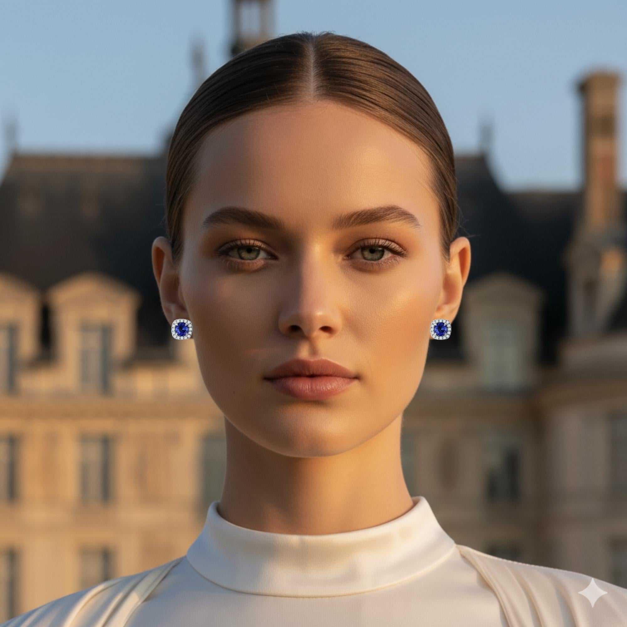 These exquisite earrings feature round sapphires at the center, glowing with deep, velvety blue brilliance. Surrounding each gem is a cushion-shaped halo frame of luminous round diamonds, adding soft contours that enhance the sapphire’s natural