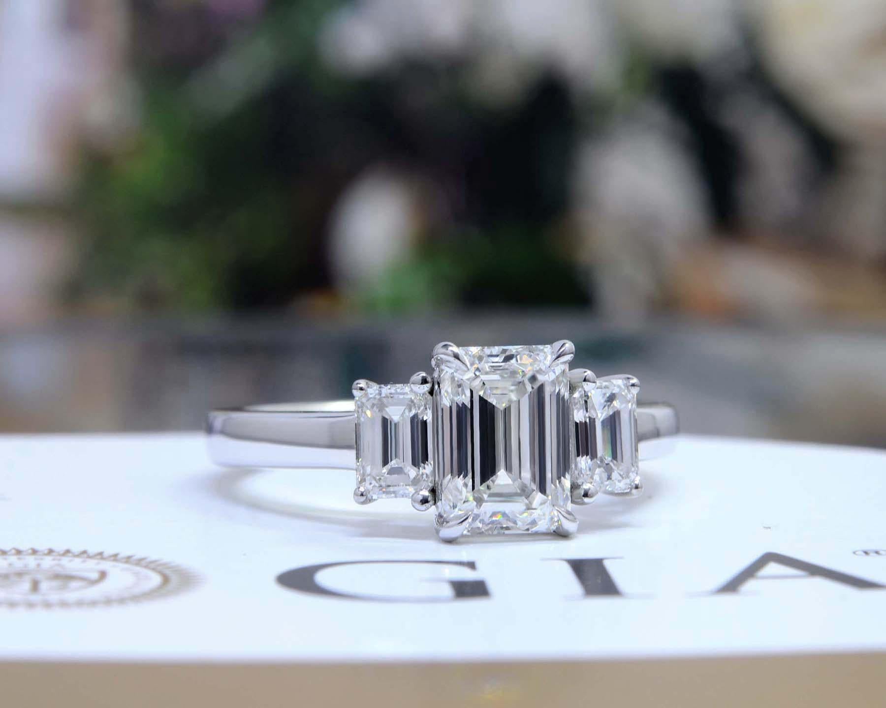 La tradition de la bague à trois pierres en diamant se perpétue dans cette bague de fiançailles exquise. Au centre de cette merveilleuse pièce se trouve un étincelant diamant taille émeraude d'un poids de 1,50 carat. Ce diamant a une pureté de Vvs1