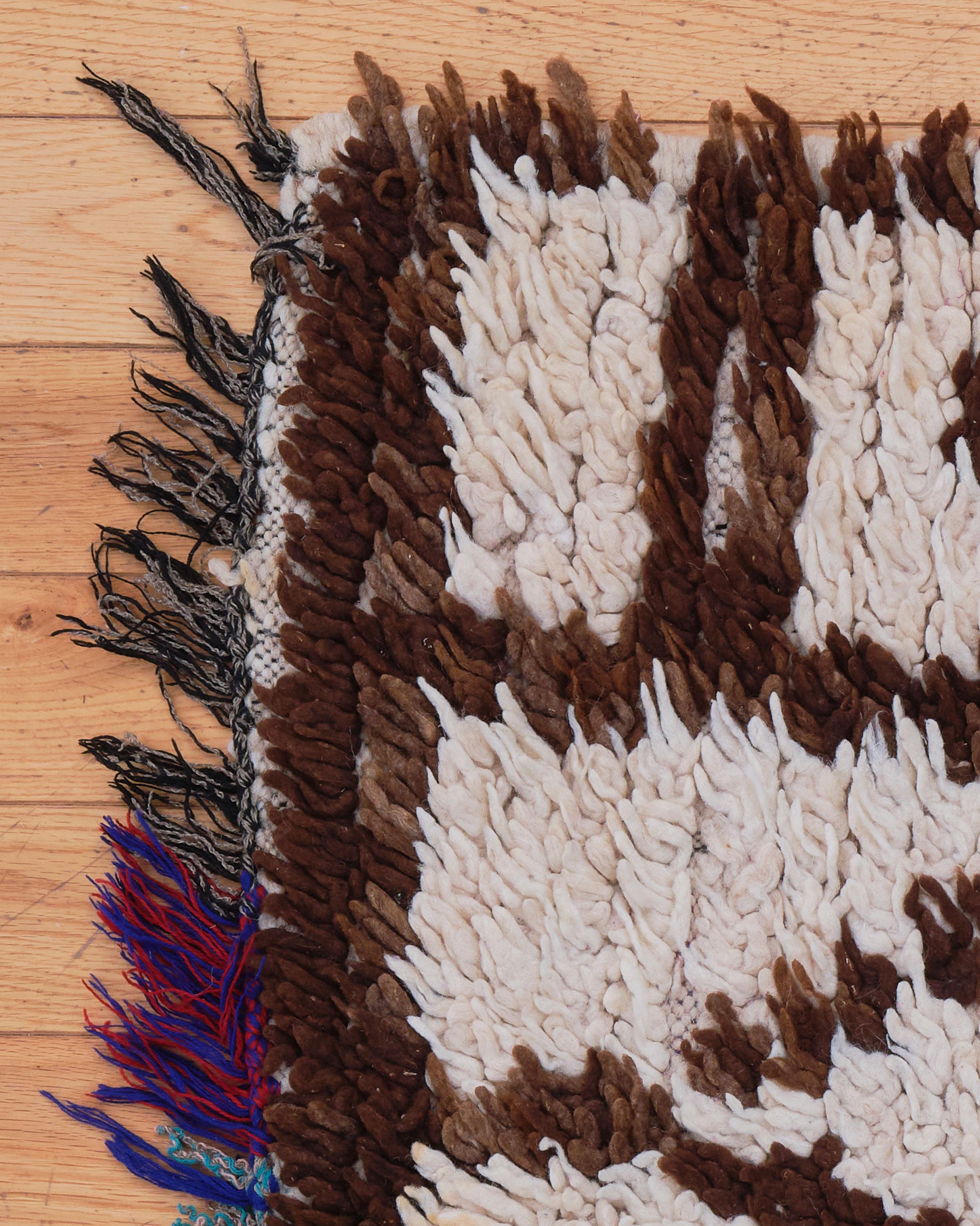 Lilium es una encantadora alfombra marroquí vintage que combina la artesanía tradicional con tonos cálidos y terrosos. Tejida a mano por artesanos bereberes, esta pequeña pieza presenta una suave base de color crema acentuada con ricos motivos