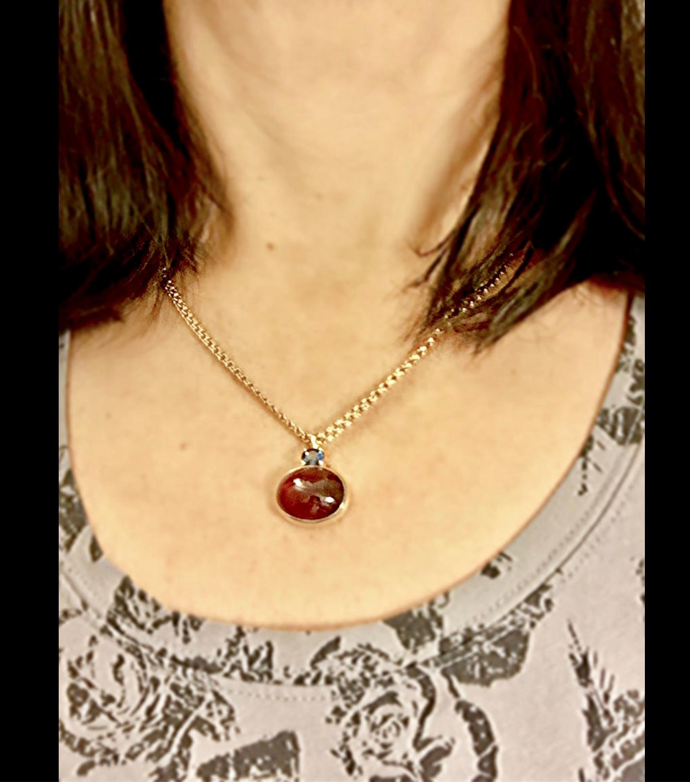 Lovely red Sapphire cabochon pendant, accented with an oval cut blue sapphire. 
Natural Sapphire Cabochon weight 20 Carats, Average Color/Clarity :Red/ SI
Second Stone: Blue Sapphire 1.00 Carat
Pendant Measurement: 27.00mm x 18.89mm, rising