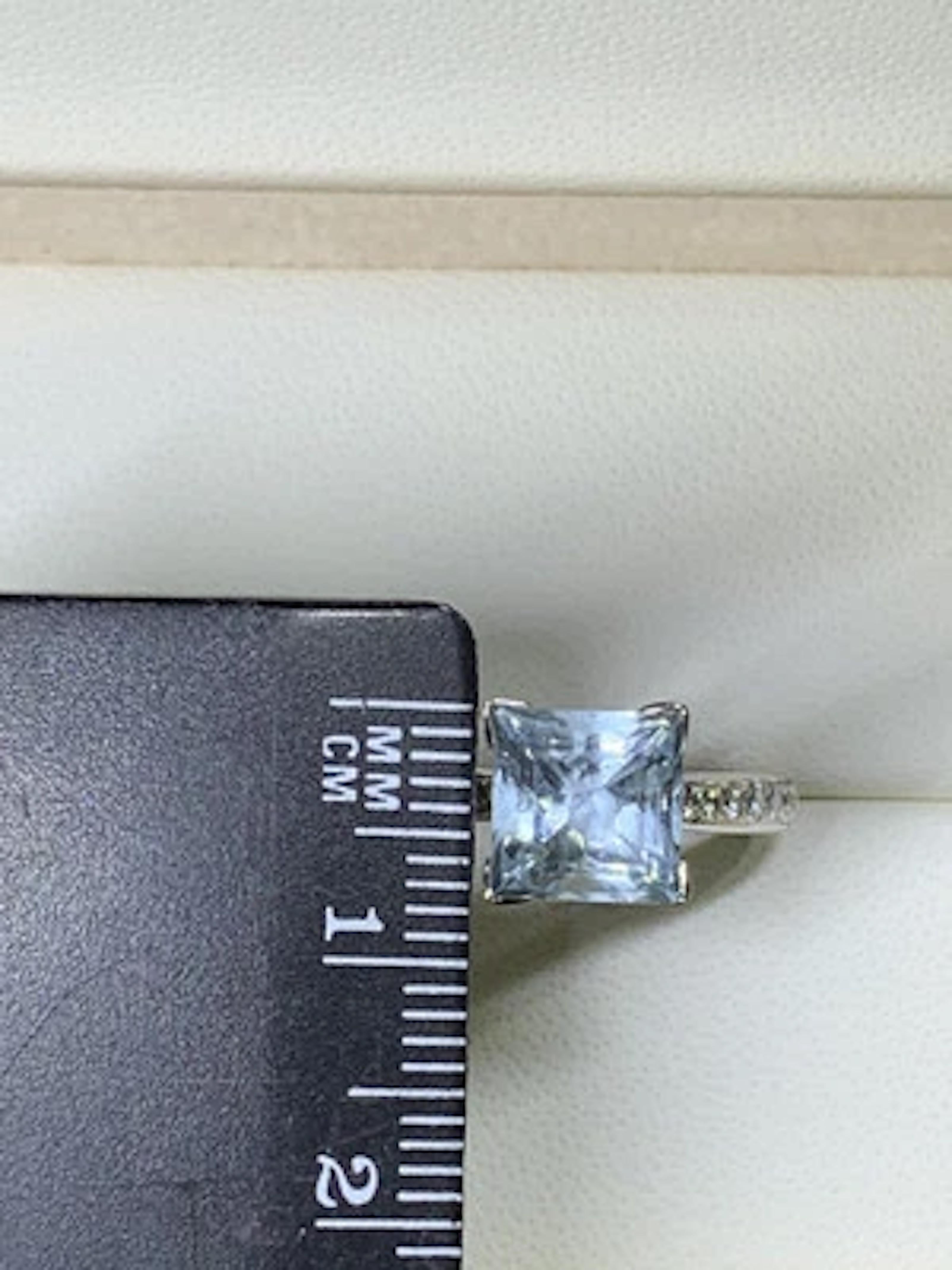 Si tratta di uno splendido anello di fidanzamento con acquamarina e diamanti da 2,10 carati taglio principessa realizzato in oro bianco 18 carati. L'anello presenta una splendida pietra principale di acquamarina blu e scintillanti diamanti bianchi.