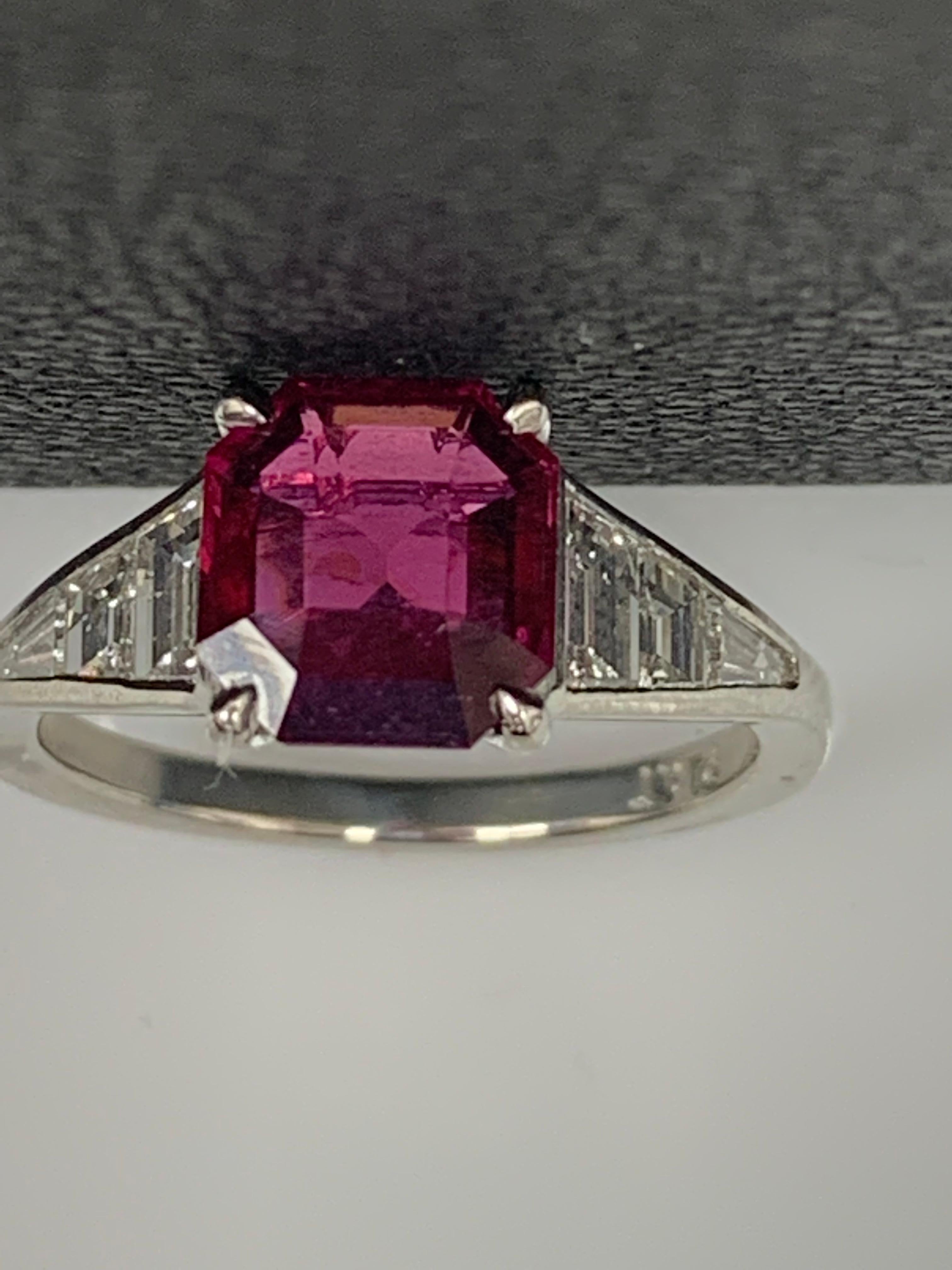 A stunning well-crafted engagement ring showcasing a 2.11-carat Emerald Cut Ruby. Flanking the center diamond are perfectly matched graduating step-cut diamonds, channel set in a polished platinum mounting. 6 Accent diamonds weigh 0.58 carats in