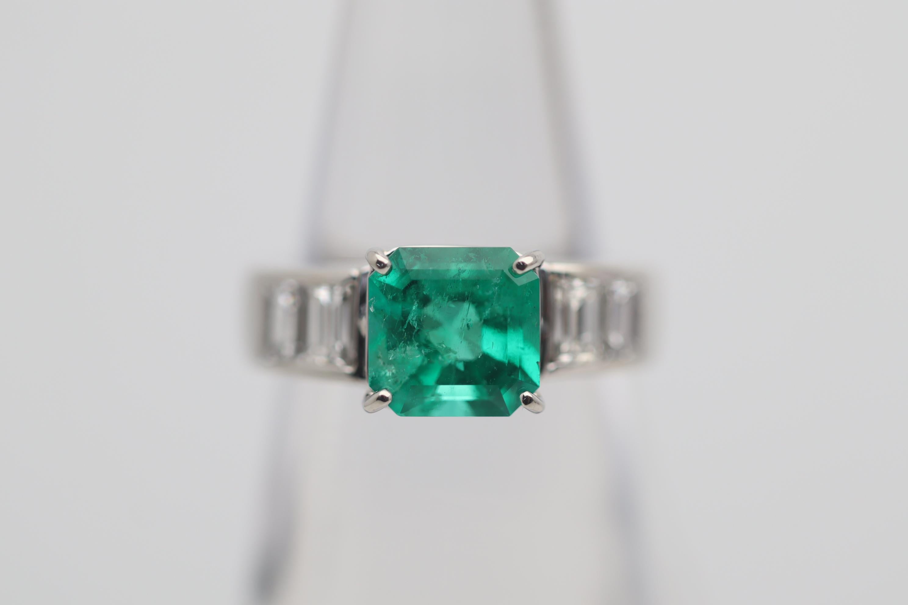An elegant and chic platinum ring featuring a fine emerald weighing 2.12 carats. It has a rich and bright grass green color along with a traditional emerald-cut shape. It is accented by 4 large baguette-cut diamonds set on its sides and weighing a
