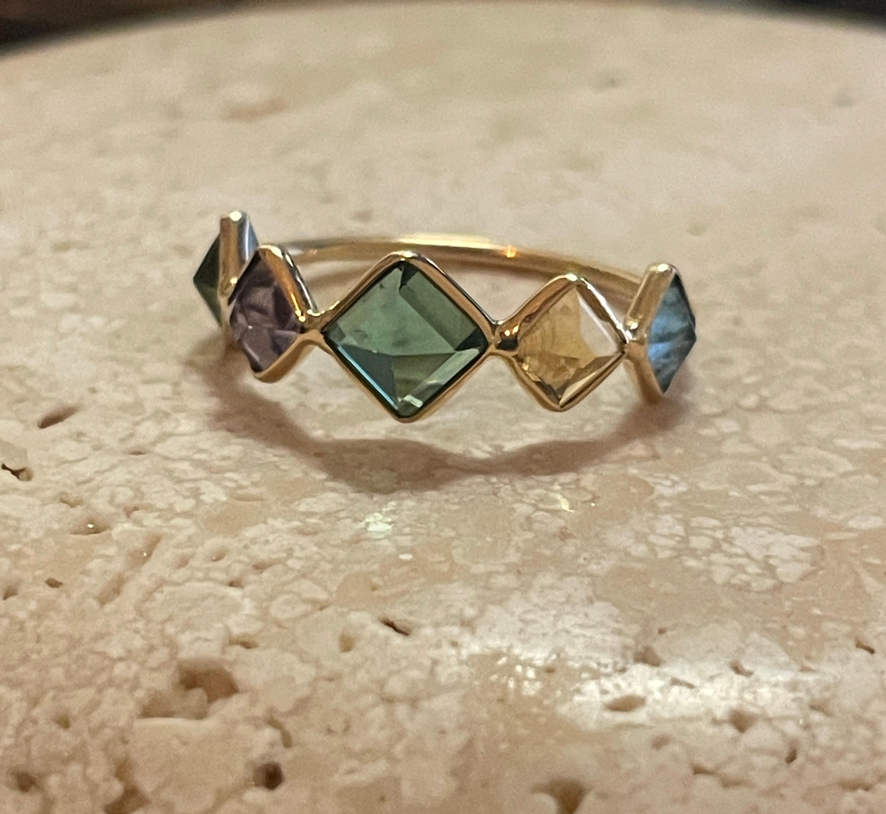 This beautiful and unique ring is comprised of 5 gemstones including Green Tourmaline, Yellow Tourmaline, Amethyst & Aquamarine. These gemstones are emerald cut and bezel set upside down in 18K gold. The upside down setting in a diamond shape makes