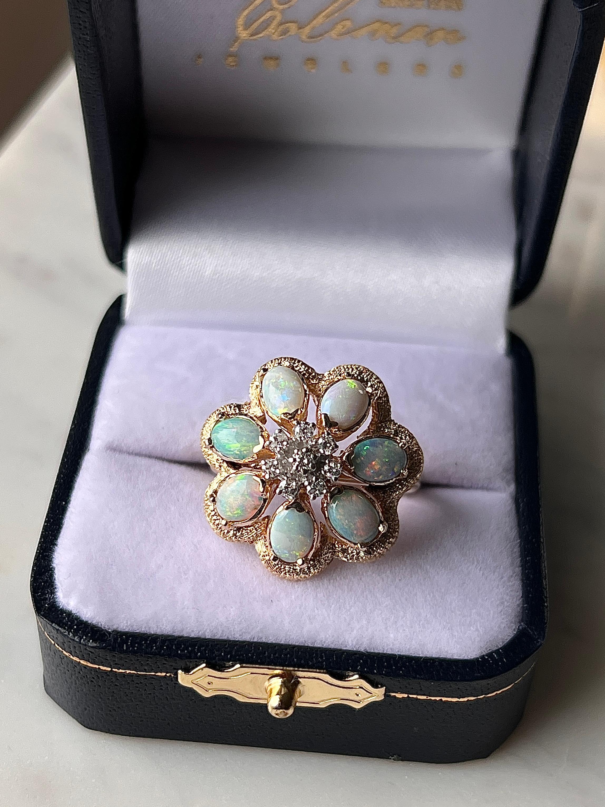 Questo incantevole anello floreale degli anni '60 è realizzato in oro giallo 14 carati e incastonato con sette luminosi opali ovali per un totale di circa 2,13 carati. Ogni opale mostra vibranti lampi di verde, blu e arancione, elegantemente