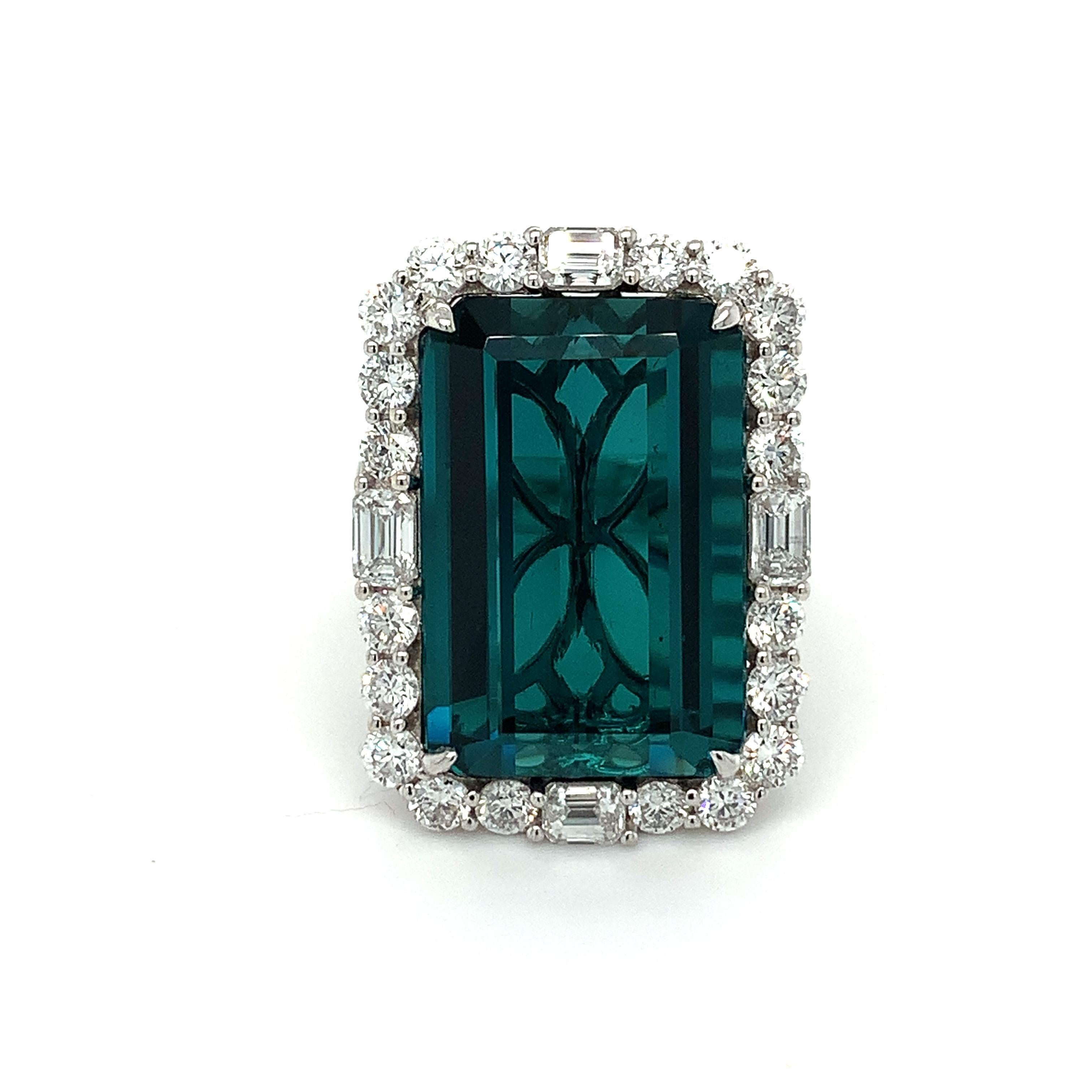 This stunning ring boasts 21.33 carat Octagonal Indicolite Tourmaline as a center stone surrounded by sparkling halo of 2.56 carat white round and baguette diamonds. The ring is hand crafted with the classic four prongs and three stripe pave diamond