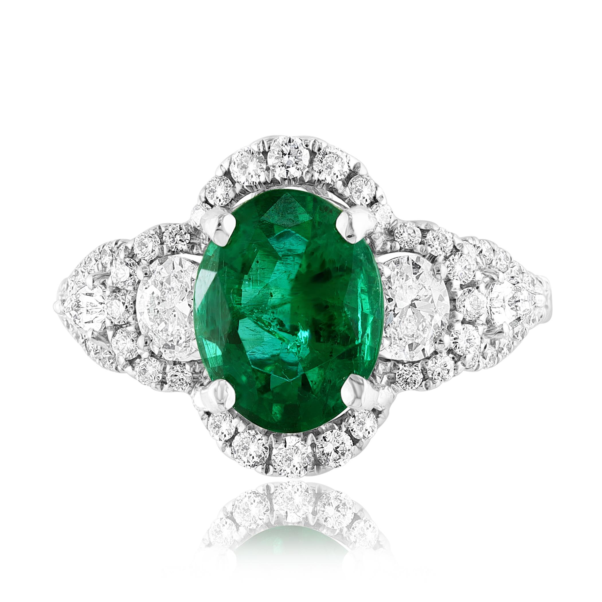 A stunning ring showcasing a rich green oval cut emerald weighing 2.15 carats surrounded by diamonds. Flanking the center stone are brilliant cut 2 round and 2 pear diamonds, weighing 0.55 carats total, framed in a brilliant diamond halo. 52 Accent