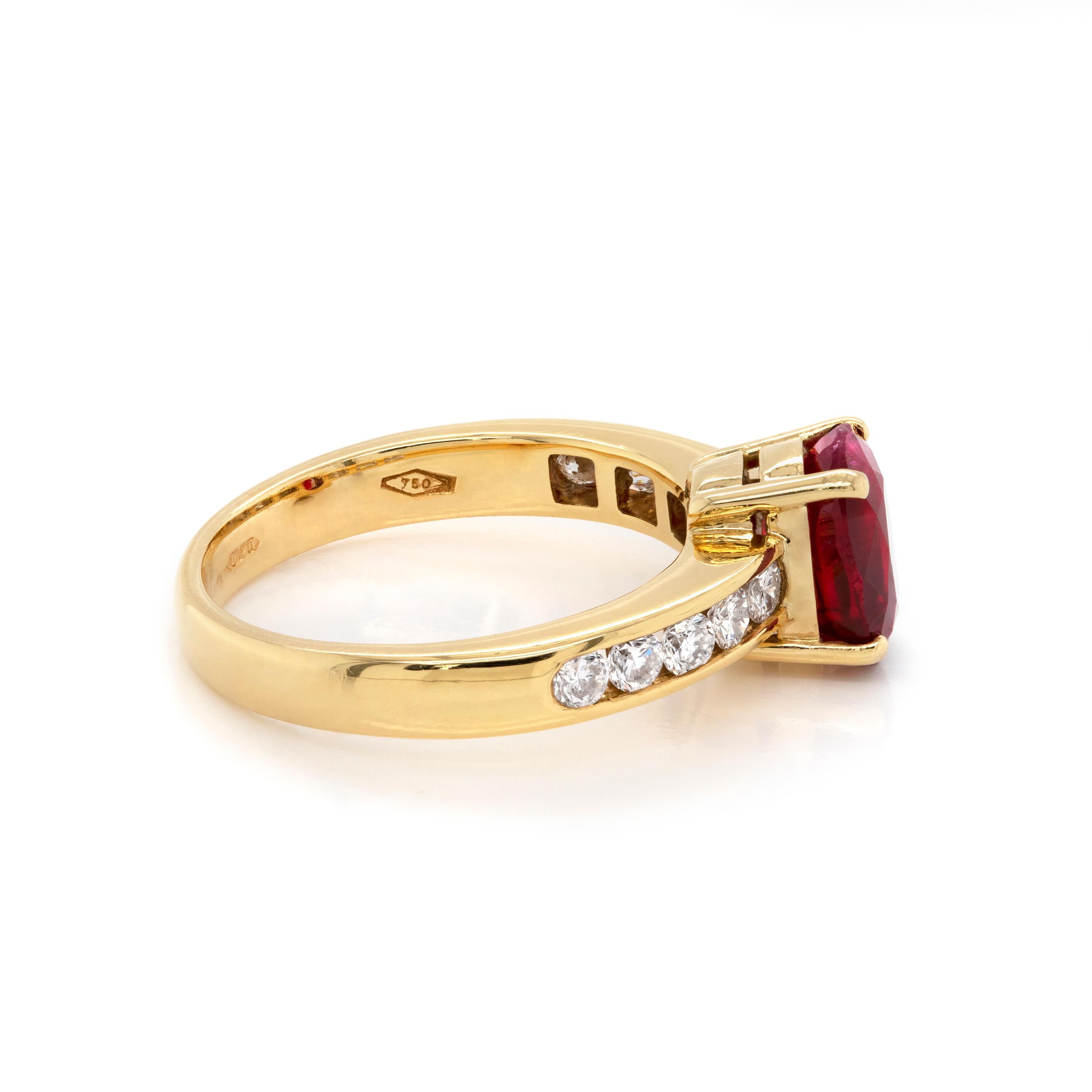 This 18 carat gold engagement ring features a wonderful 2.15ct lively red oval ruby in the centre, mounted in an open back, four claw setting. The ruby is accompanied by five channel set round brilliant cut diamonds on either side, weighing an