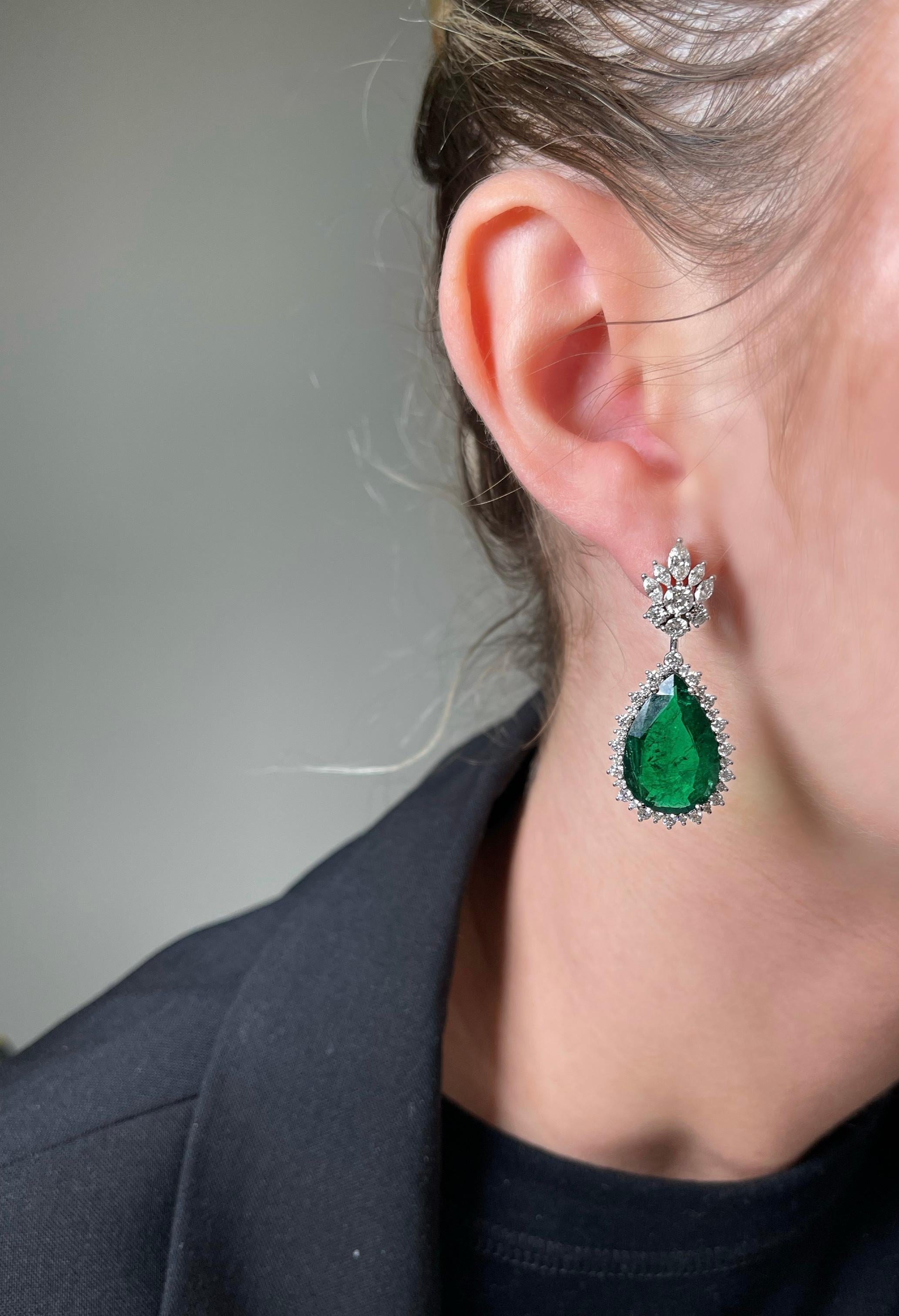 Introducing an exquisite set of Natural Emerald and Diamond Earrings, a true testament to elegance and sophistication. Each earring features a mesmerizing Vivid Green Zambian Emerald, skillfully cut into a captivating pear shape, boasting an